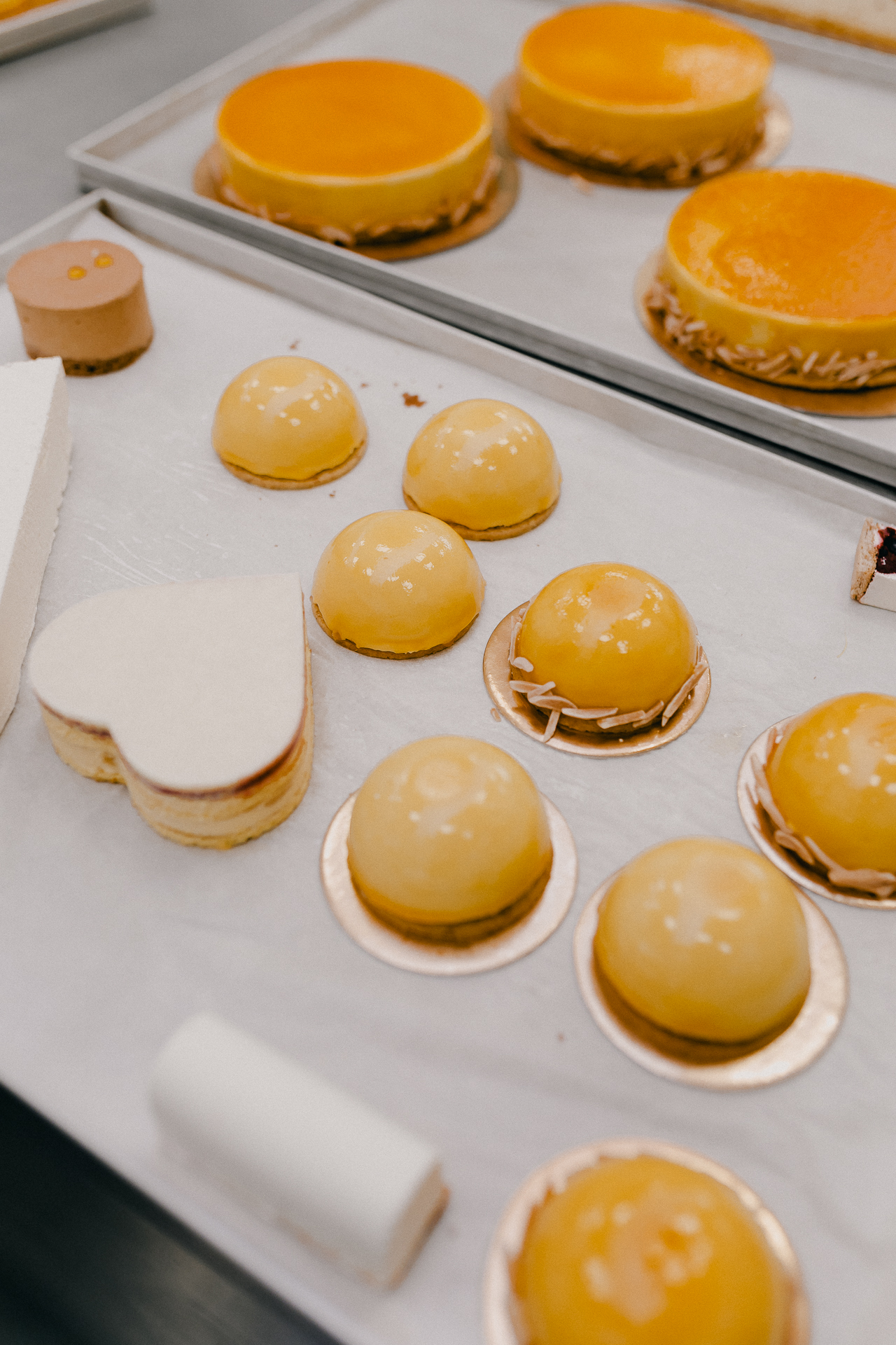 Giotto Bakery – A tray of tiny shiny desserts in various shapes set on top of rose-gold discs.