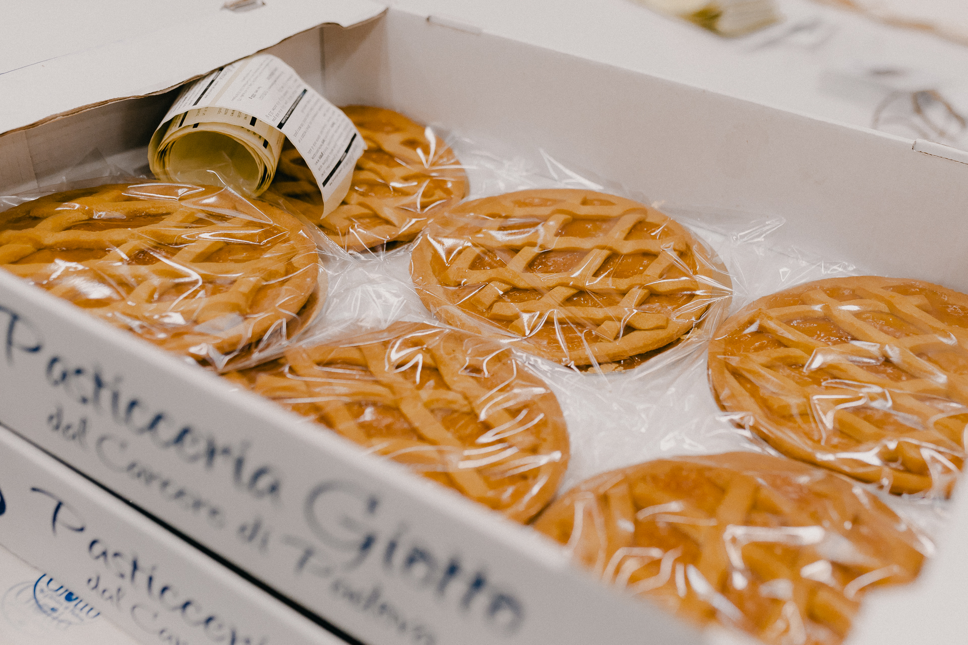 Giotto Bakery – Six crostata tarts filled with an orange-coloured jam, sitting in a box and covered with plastic foil.