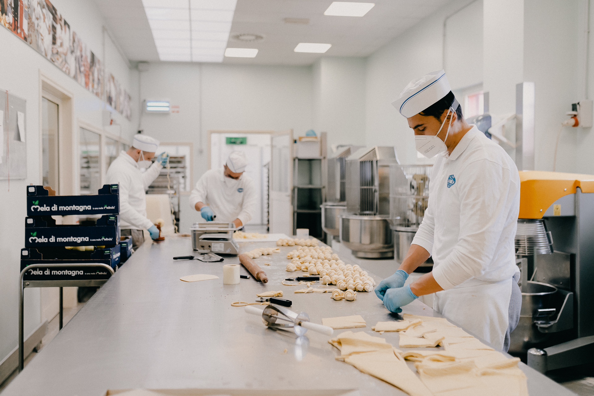 Giotto Bakery – a very long stainless steel work table where three inmates are diving croissant dough into portions and rolling it in shape.