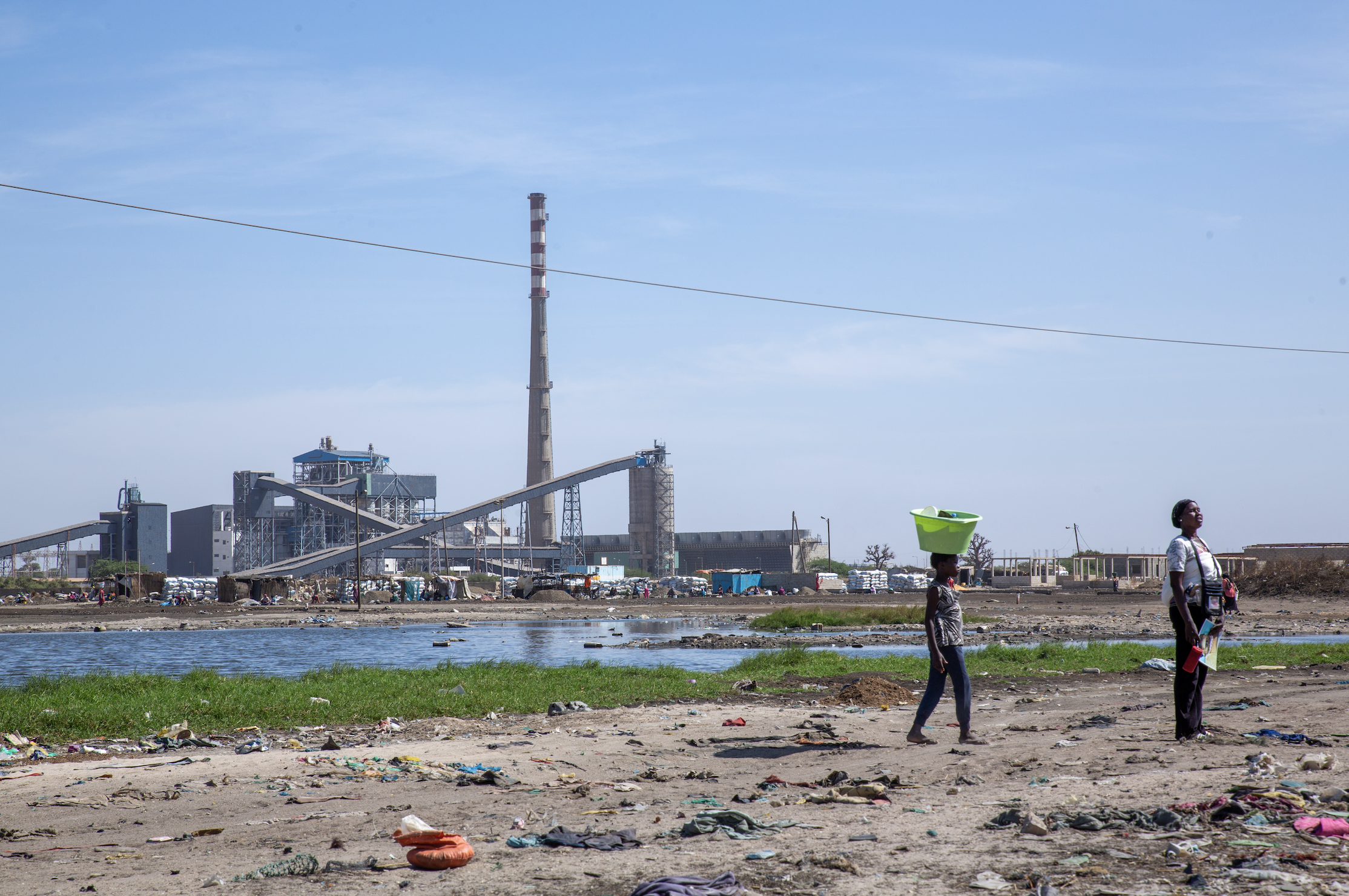 Two people stand on a road next to the Sendou plant in Bargny.