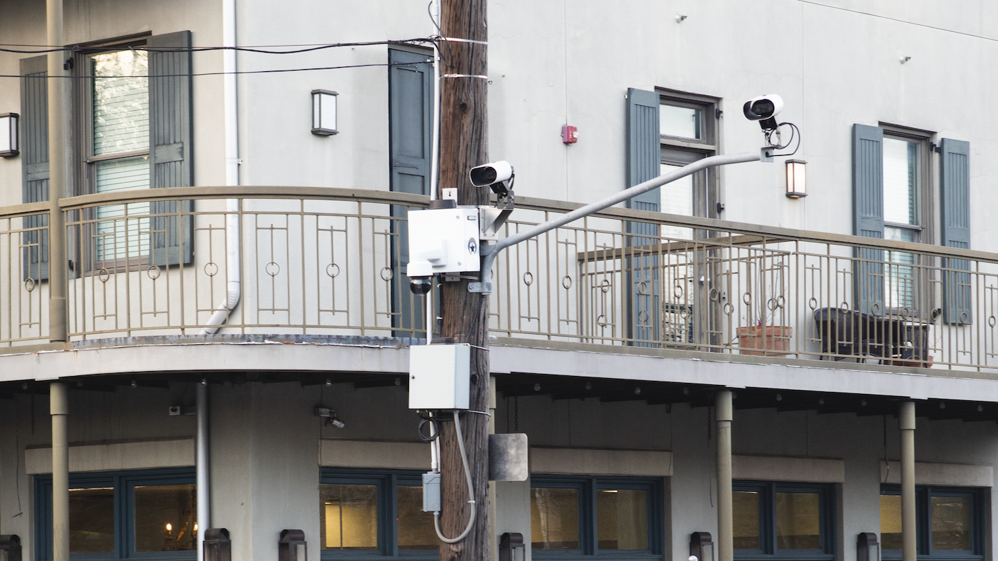 Surveillance cameras hang from a metal pole on a street corner in New Orleans.