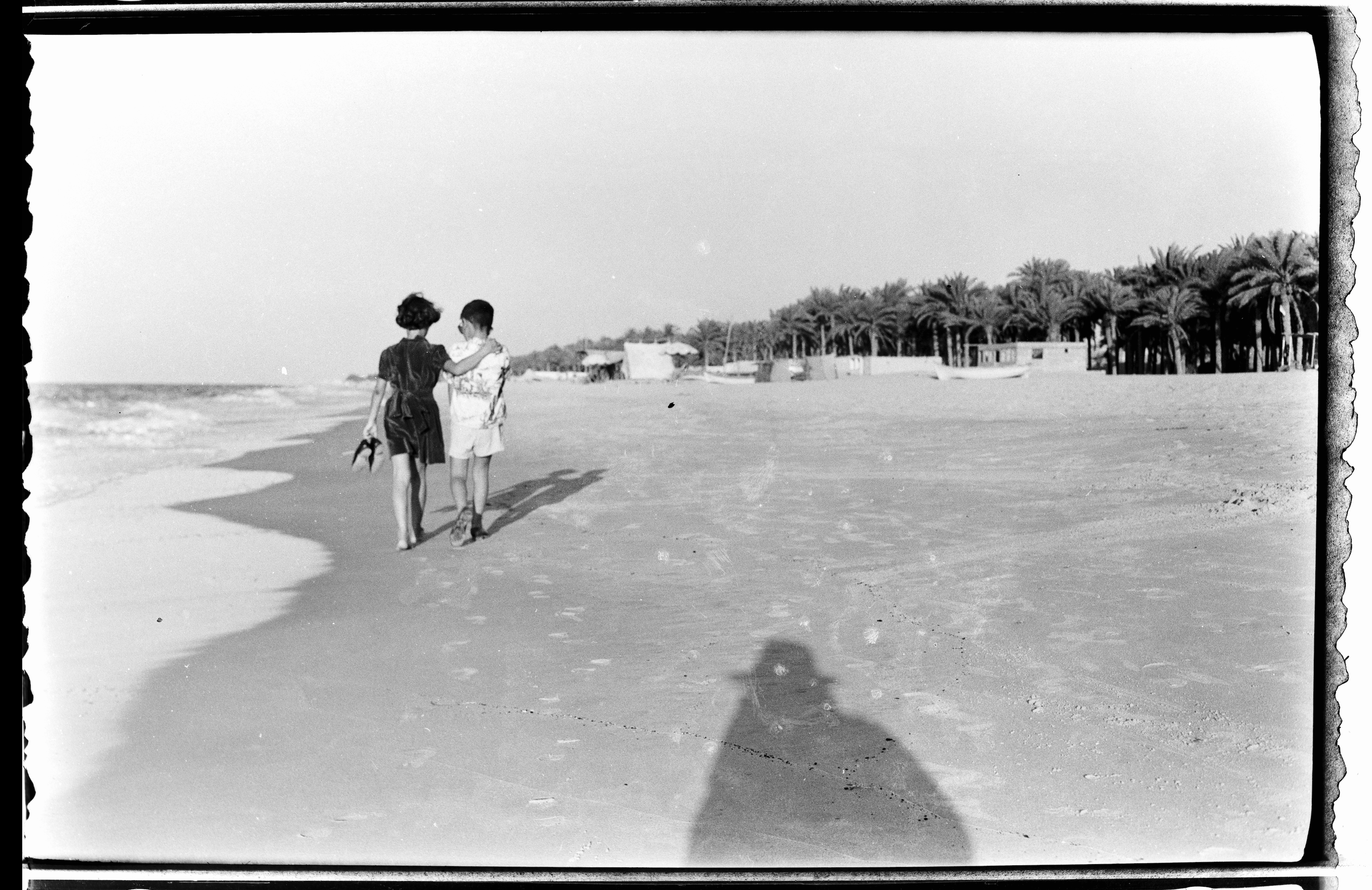 Kegham Djeghalian, Gaza photographer – man and woman walking down an empty beach lined with palm trees.