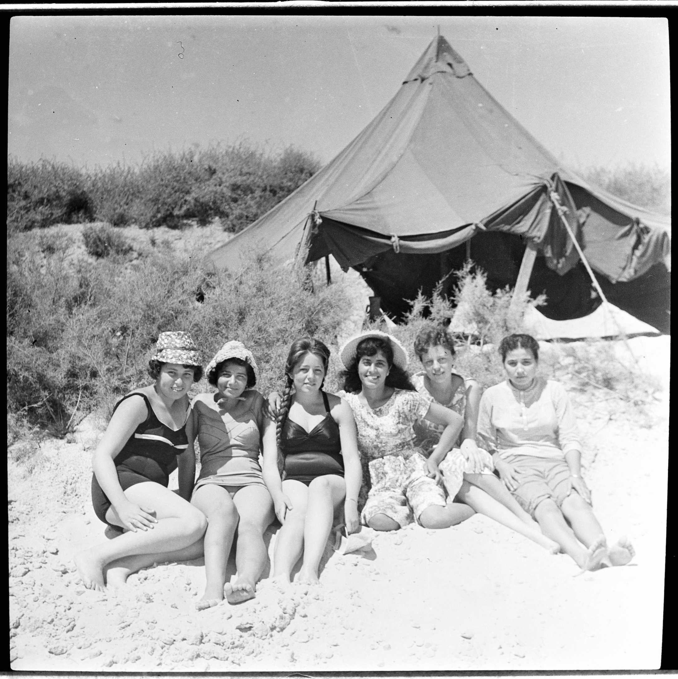 Kegham Djeghalian, Gaza photographer – Six women in bathing suits and summer clothes sitting on the beach in front of a tent.