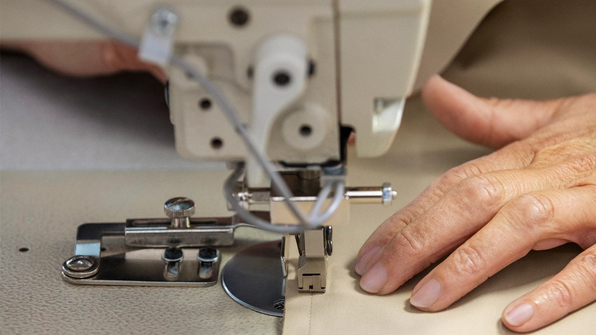 A hand passing clothe through a sewing machine