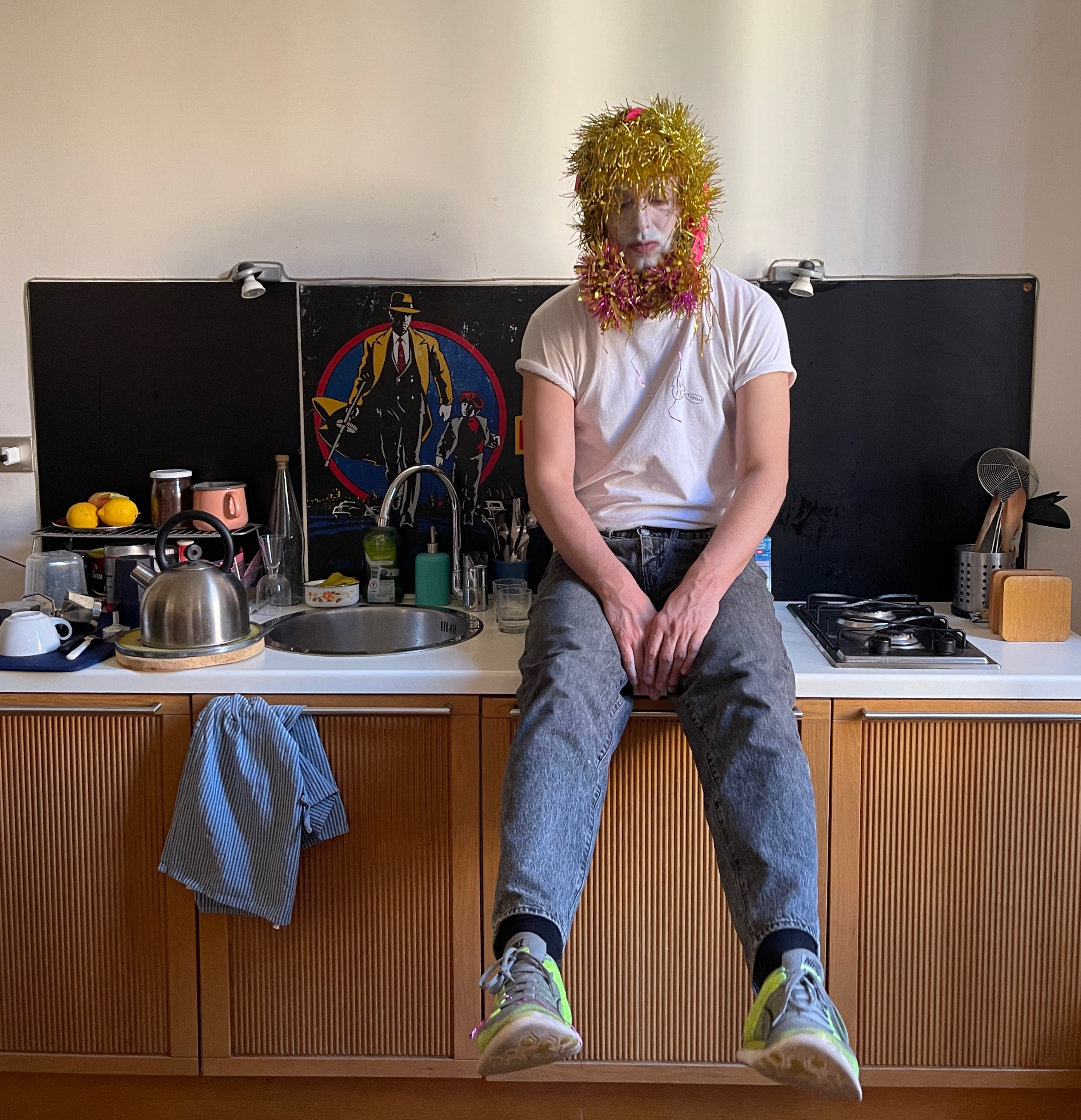 Nico Vascellari con indosso jeans, sneaker e tshirt, seduto sul mobile di una cucina nella tappa el tour IONOI in lazio