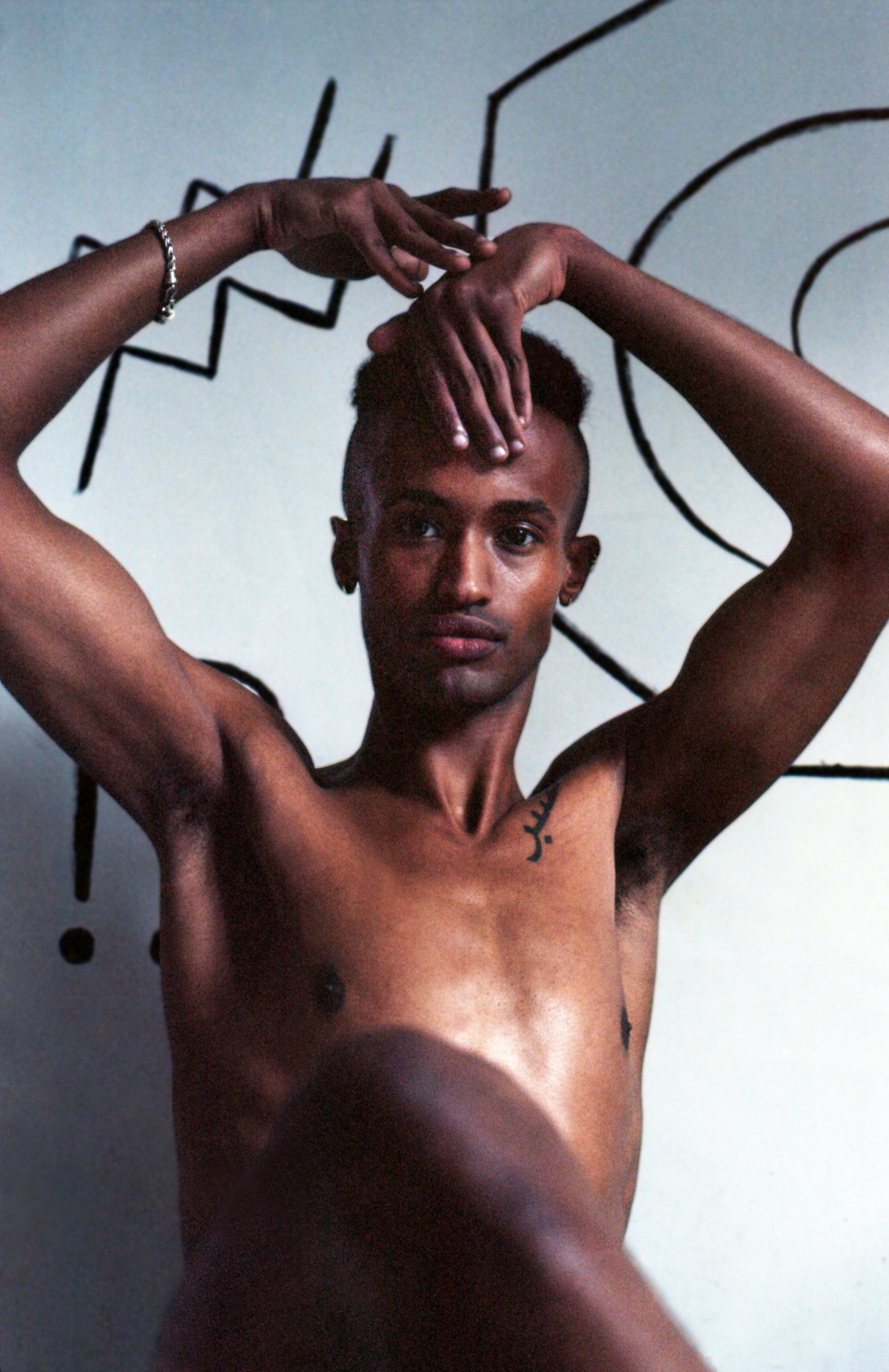 Yaqub con mano in fronte e graffiti sulla parete dietro di lui, progetto Show Me Your Queer