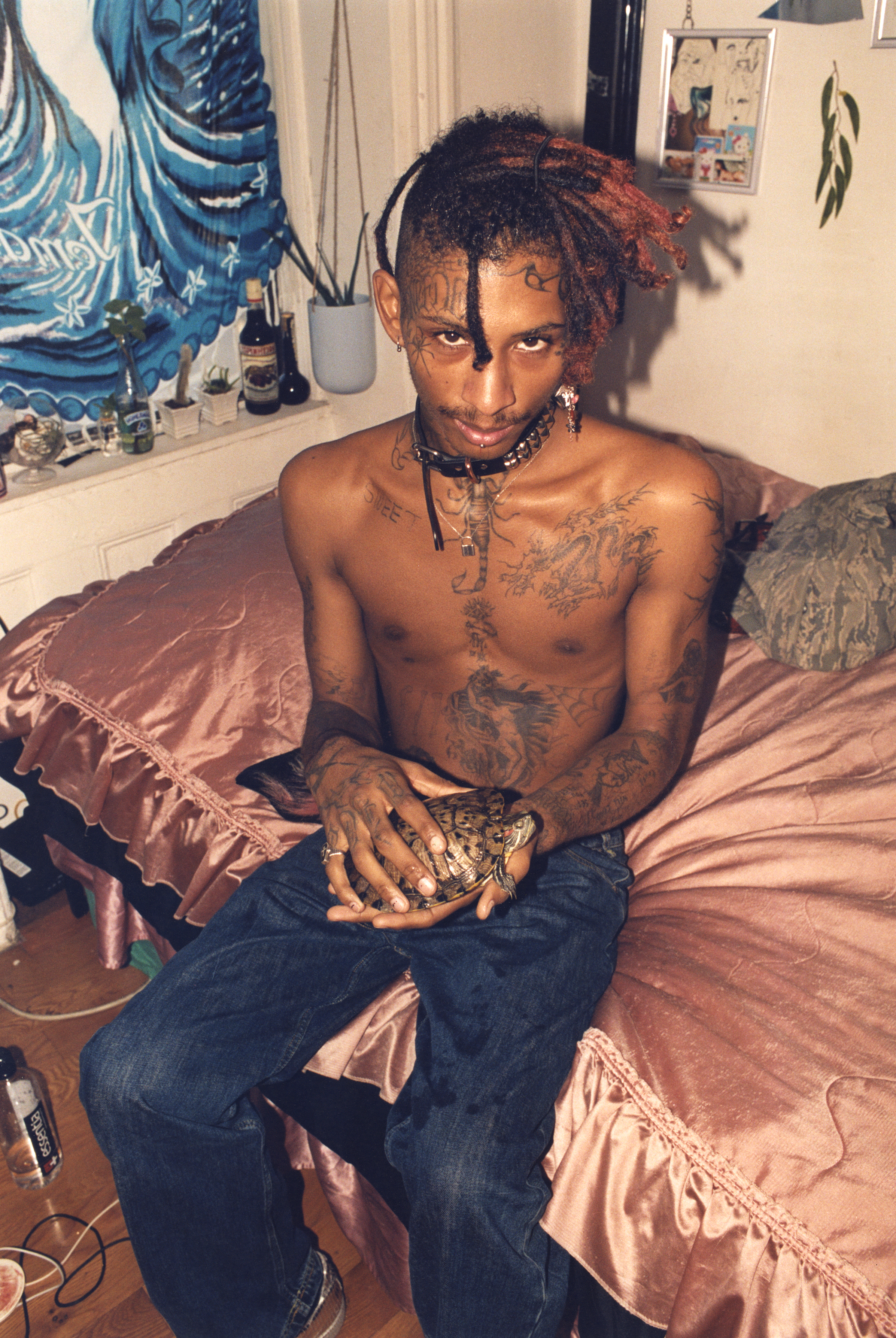 omari kirk sitting on his bed and showing off his tattoos by holding his turtle