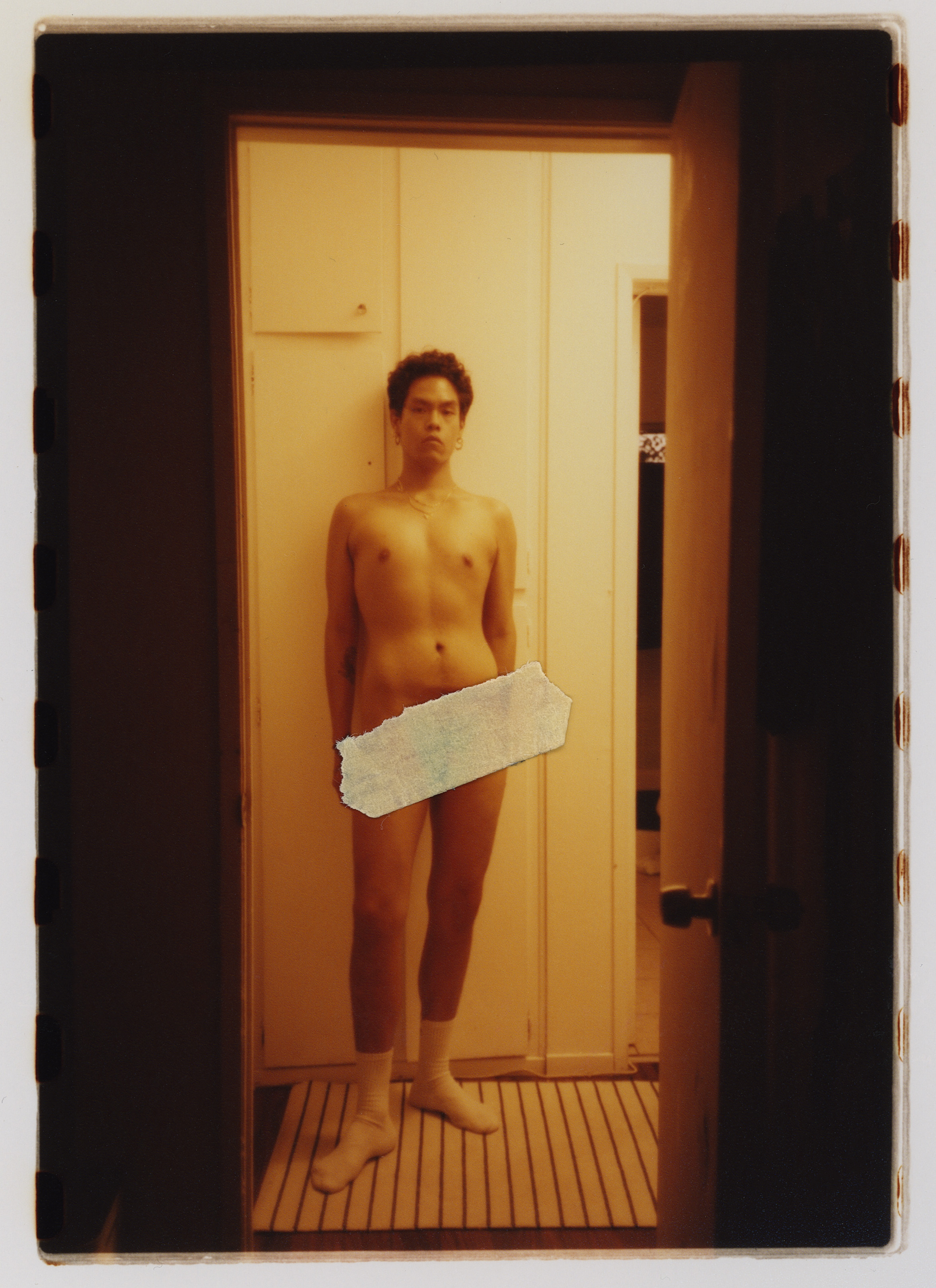 a nude person stands in the corridor of their home, looking to camera