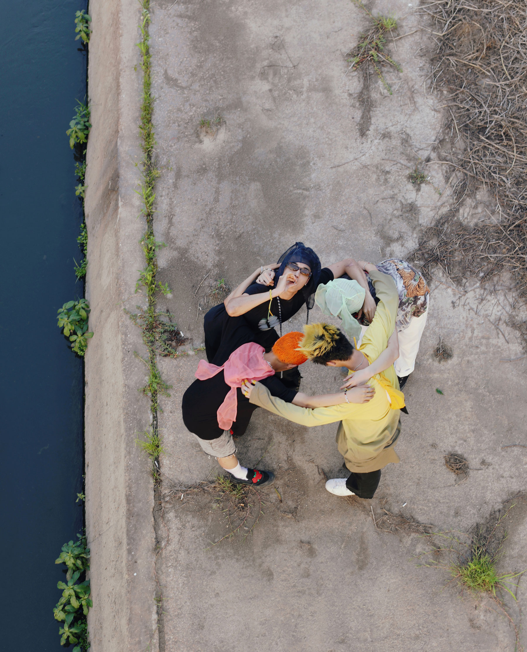 four young men with colourful hair stand in a circle with their arms around each other, shot from above