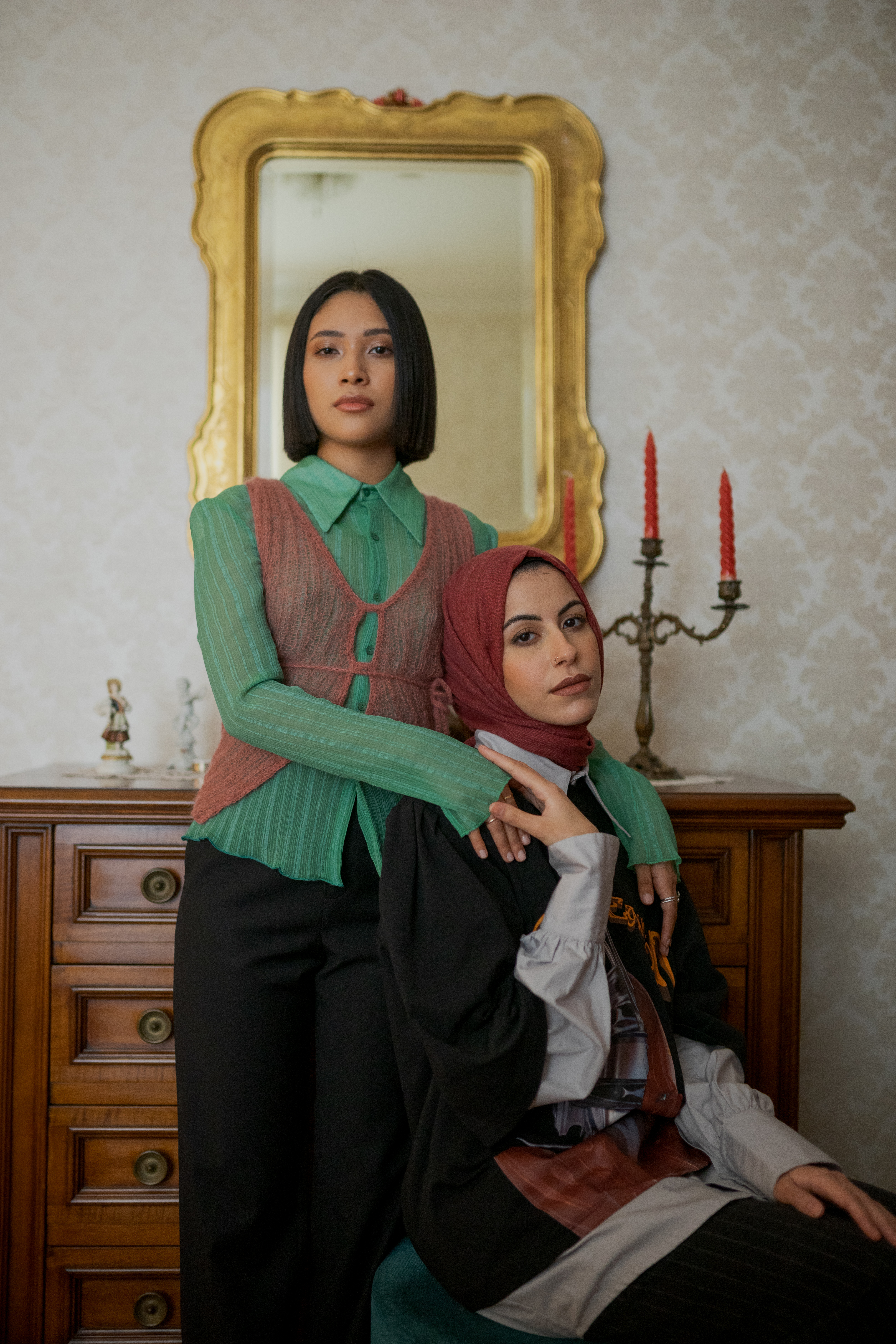 YOUTH-Torino, l'editoriale di i-D sui ragazzi di seconda generazione: Esraa e Kimberly sedute davanti a uno spiedo e a un candelabro appoggiato a un cassettone