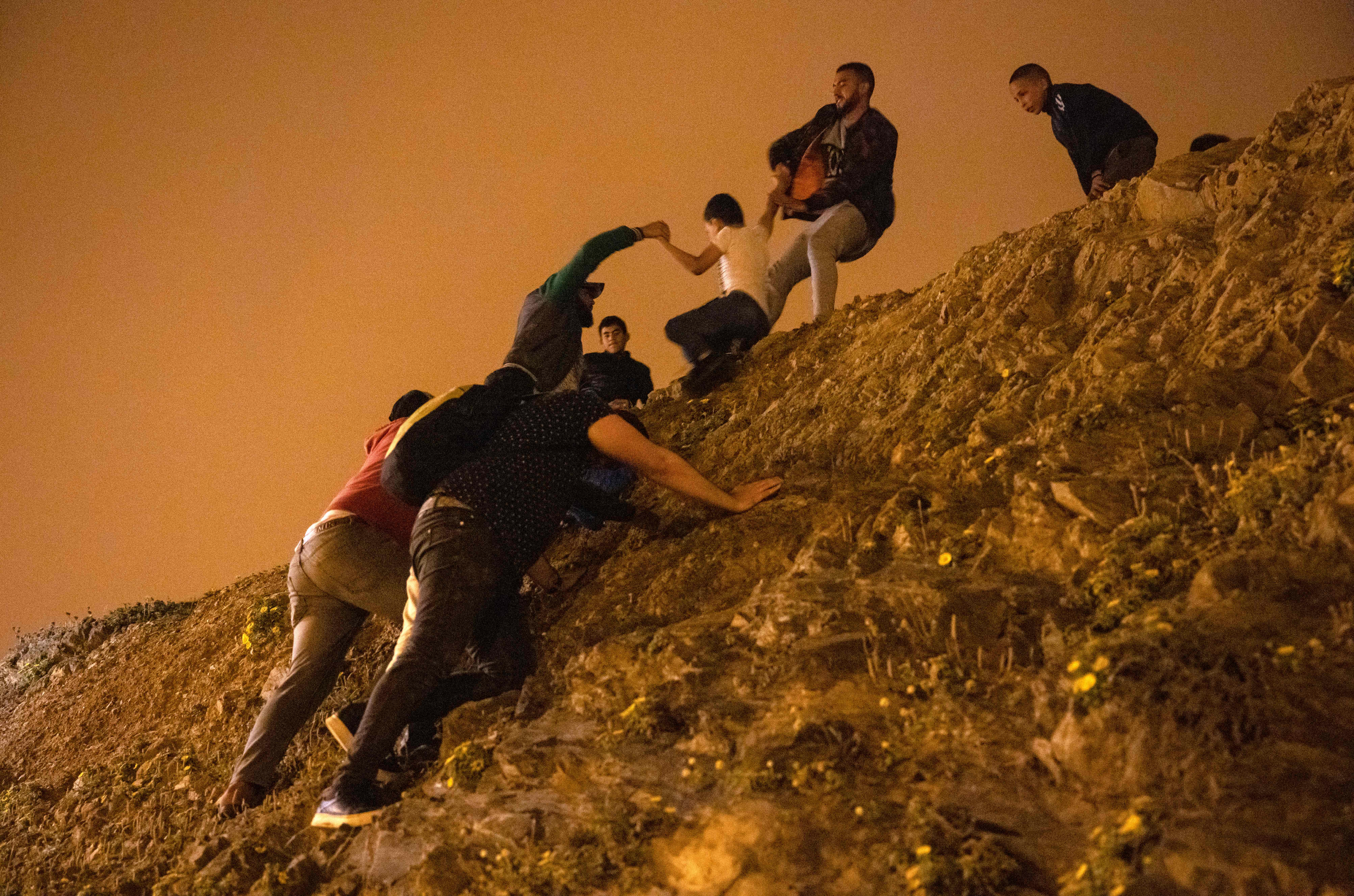 Moroccan migrants climb a rocky cliffside as they attempt to cross the border and reach Ceuta. Photo: FADEL SENNA/AFP via Getty Images