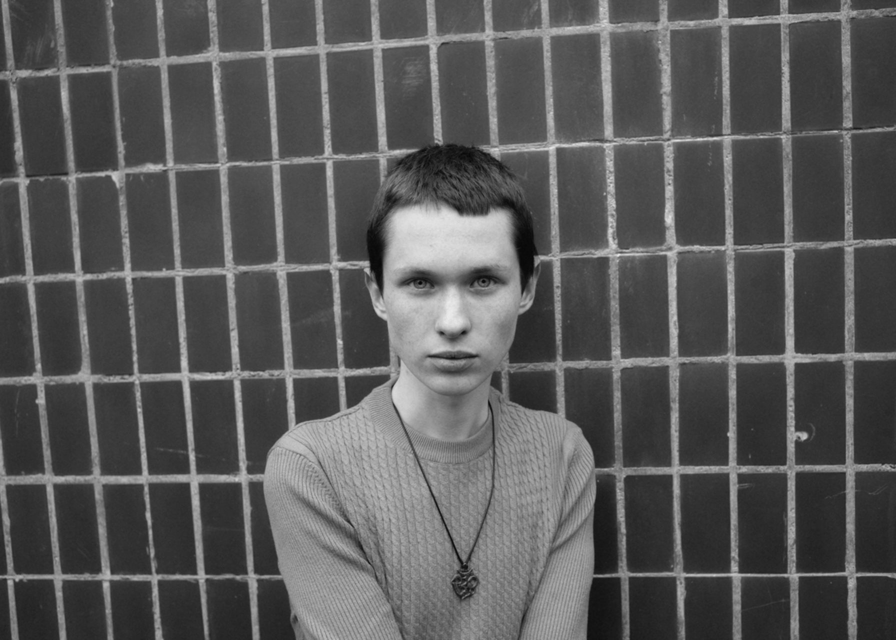 a young siberian man against a tiled wall looks into the camera