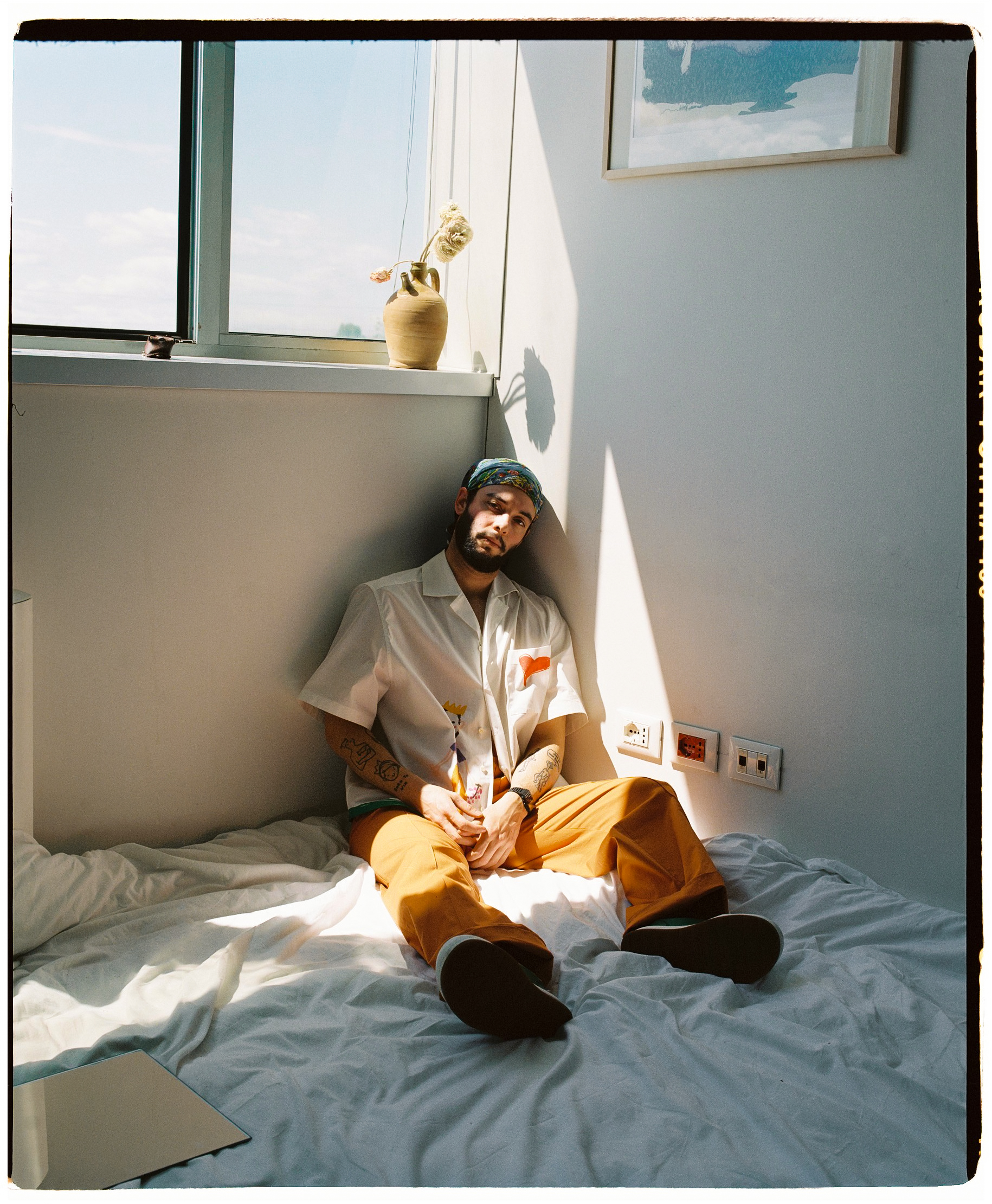 foto di francesco cicconetti mehths seduto su un letto sotto a una finestra con indosso a-o bowling shirt di Federico Cina, foto Sara lorusso