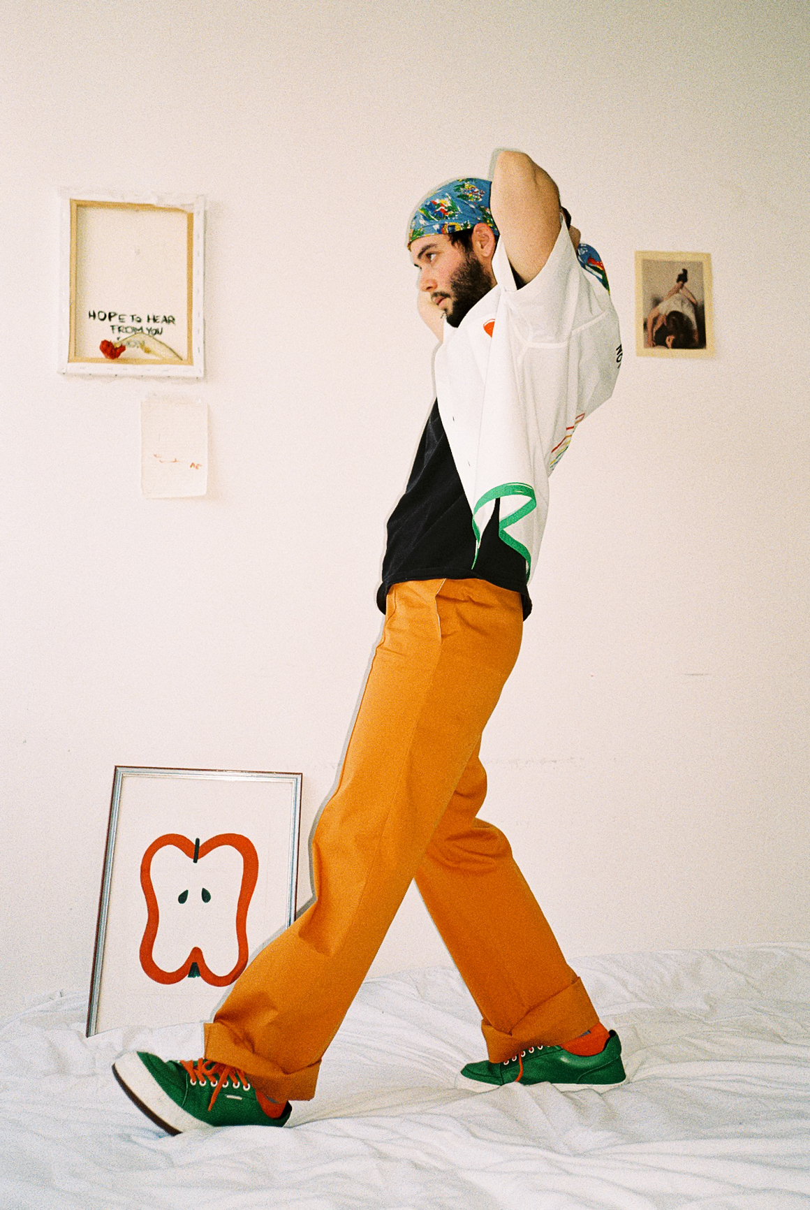 foto di Francesco Cicconetti mehths in piedi su un letto con indosso pantaloni arancio, sneaker verdi e bandana azzurra e a-o bowling shirt di Federico Cina, foto Sara lorusso