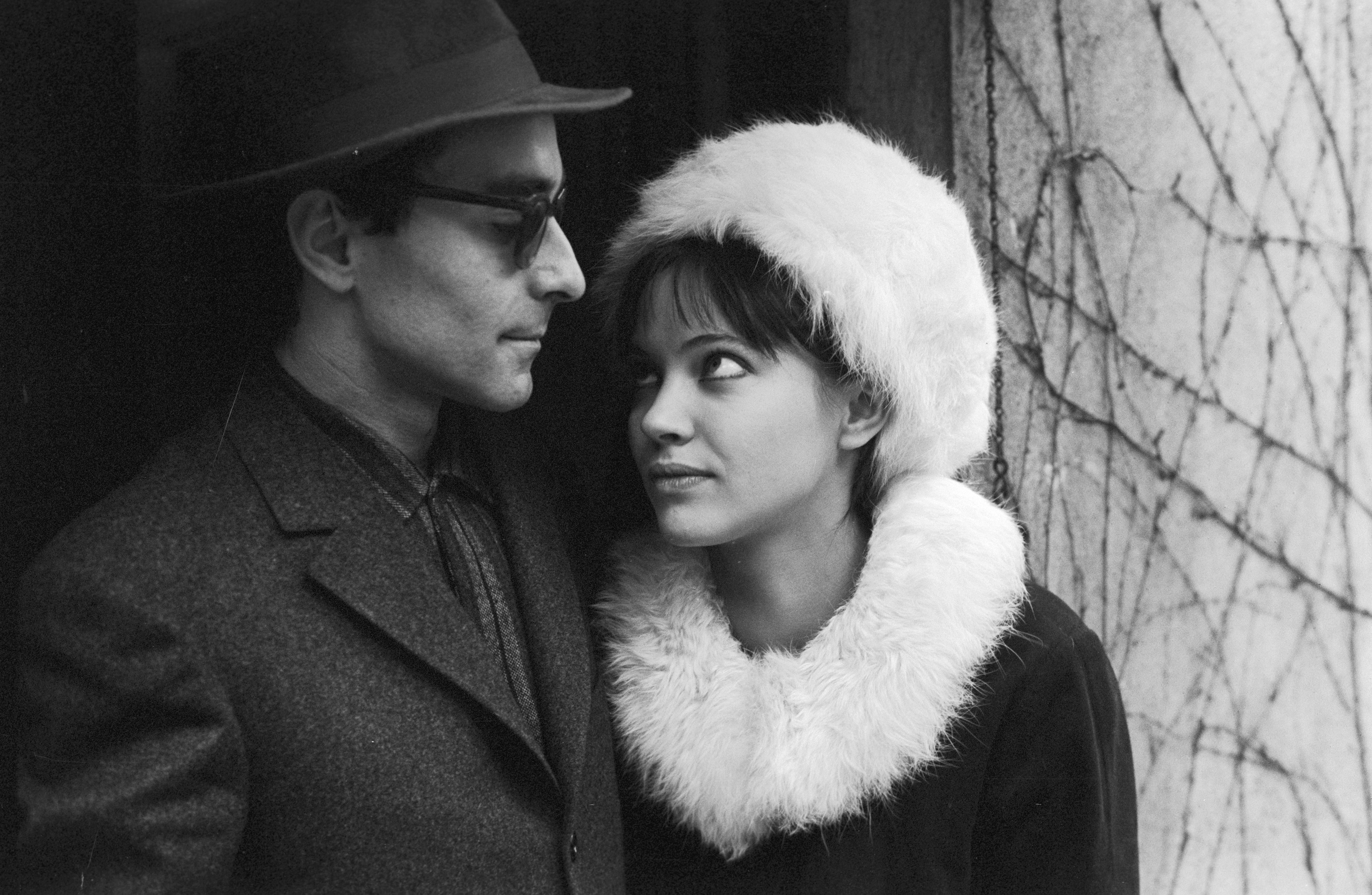anna karina looking up at jean-luc godard while wearing a fur trimmed coat and hat