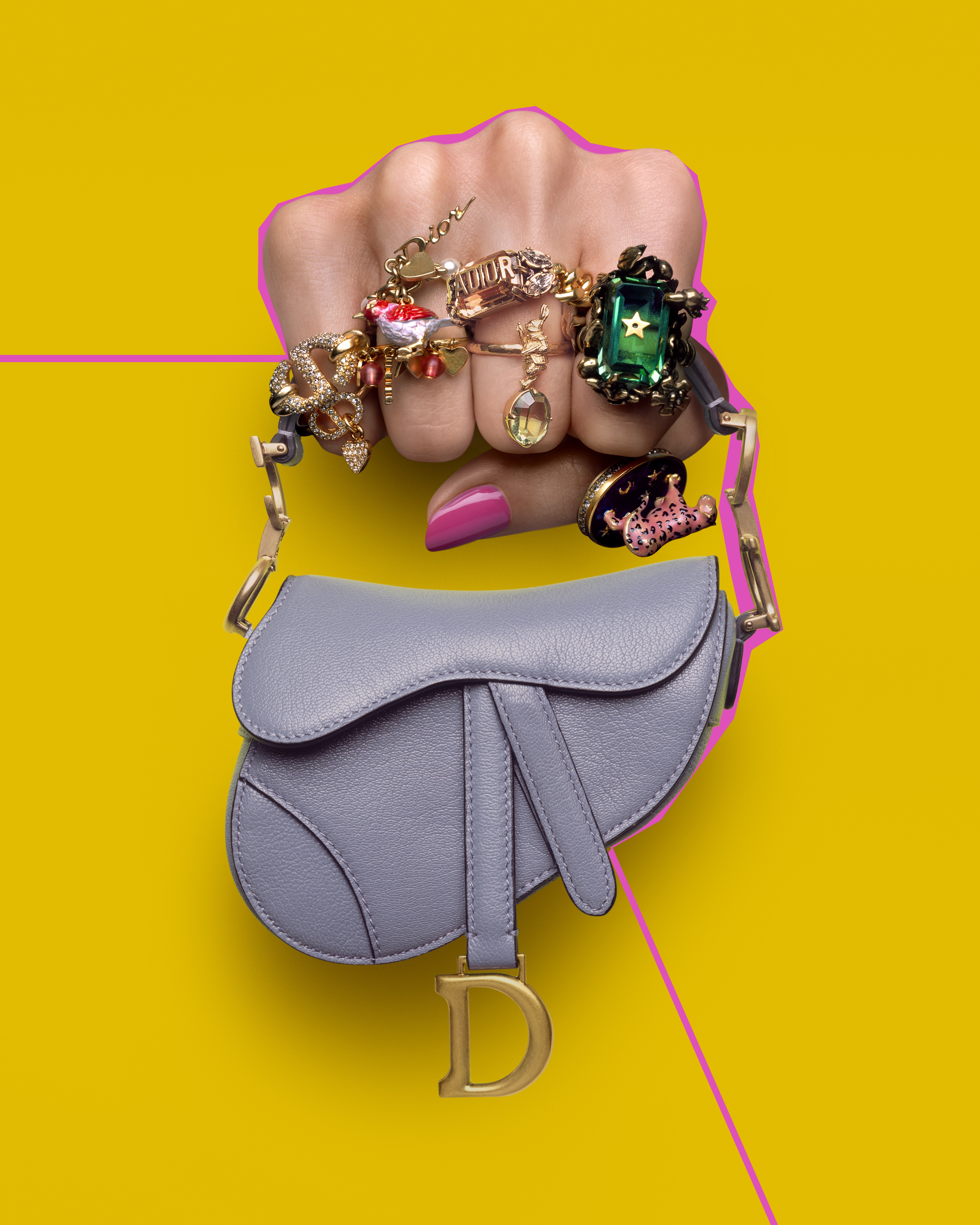 A hand wearing multiple rings clutching a miniature Dior saddle bag