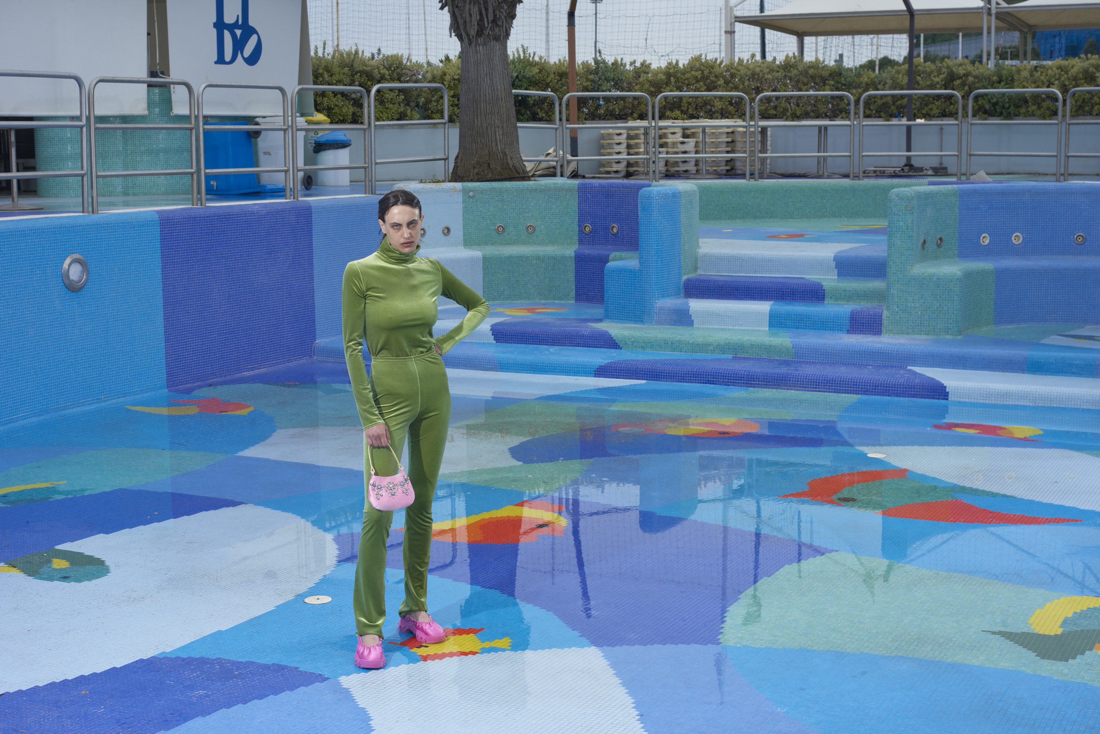 modella vestita di verde in mezzo a piscina in paesaggio post-sovietico