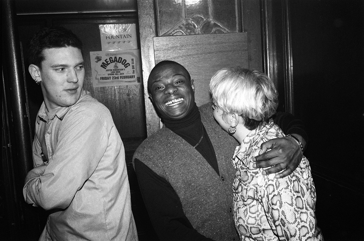 three people in a club, the man in the middle is smiling broadly
