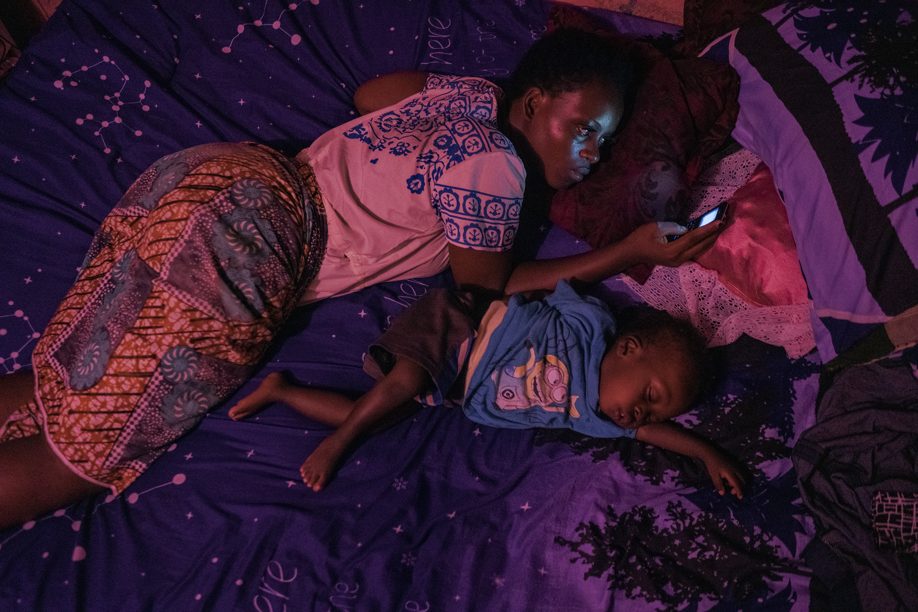 donna con bambino su un letto mentre guarda cellulare Hannah Reyes Morales