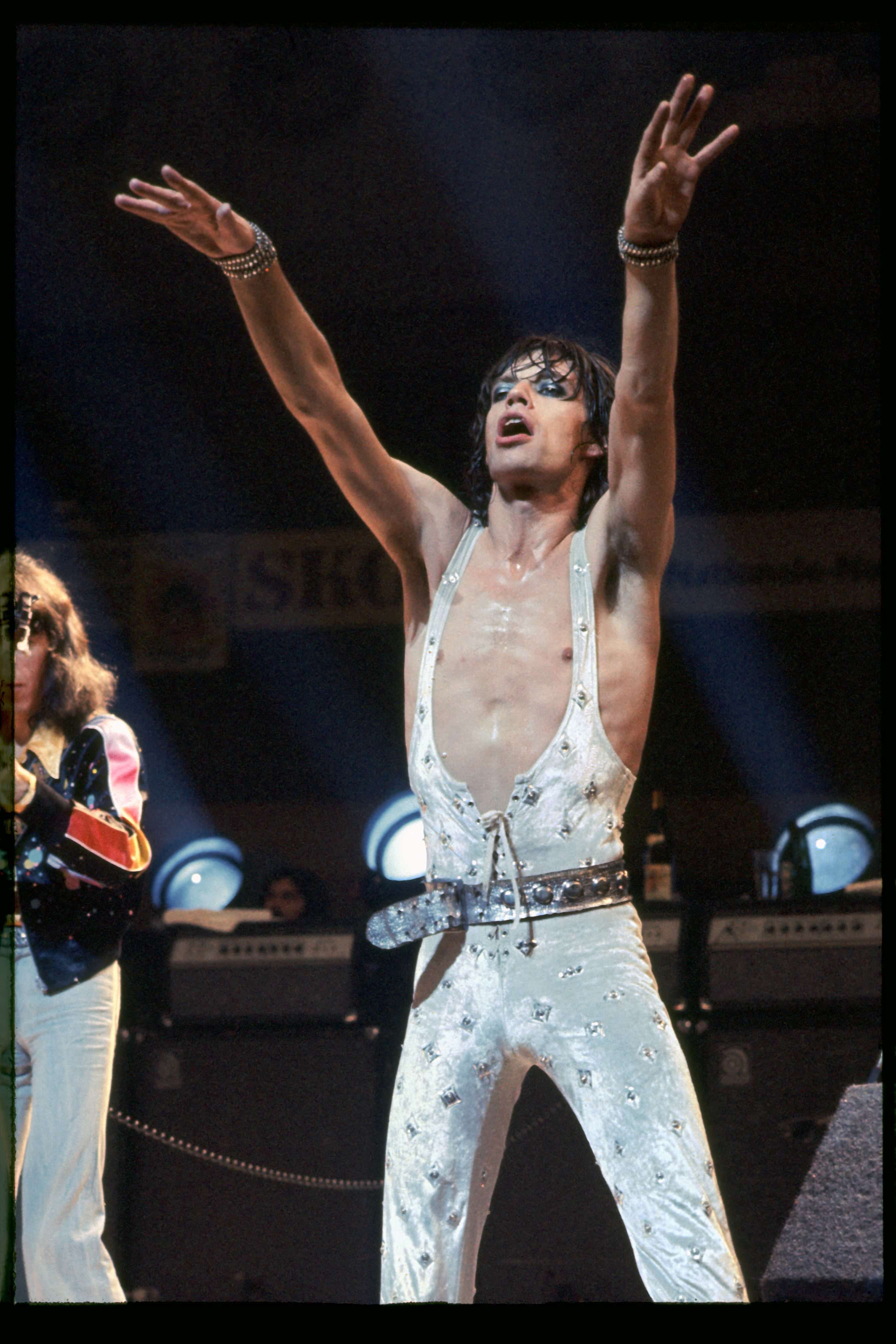 mick jagger performing in a jumpsuit and blue eyeshadow at a concert in 1973