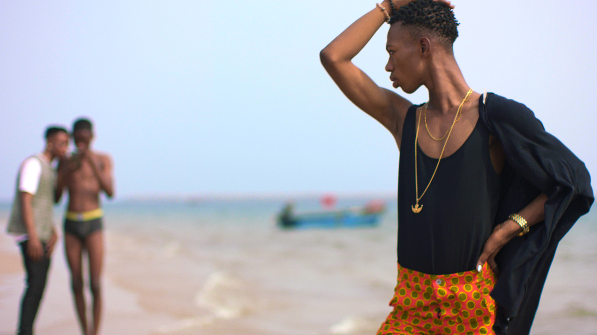 a person on a beach, arm to their head looking over at two figures in the background