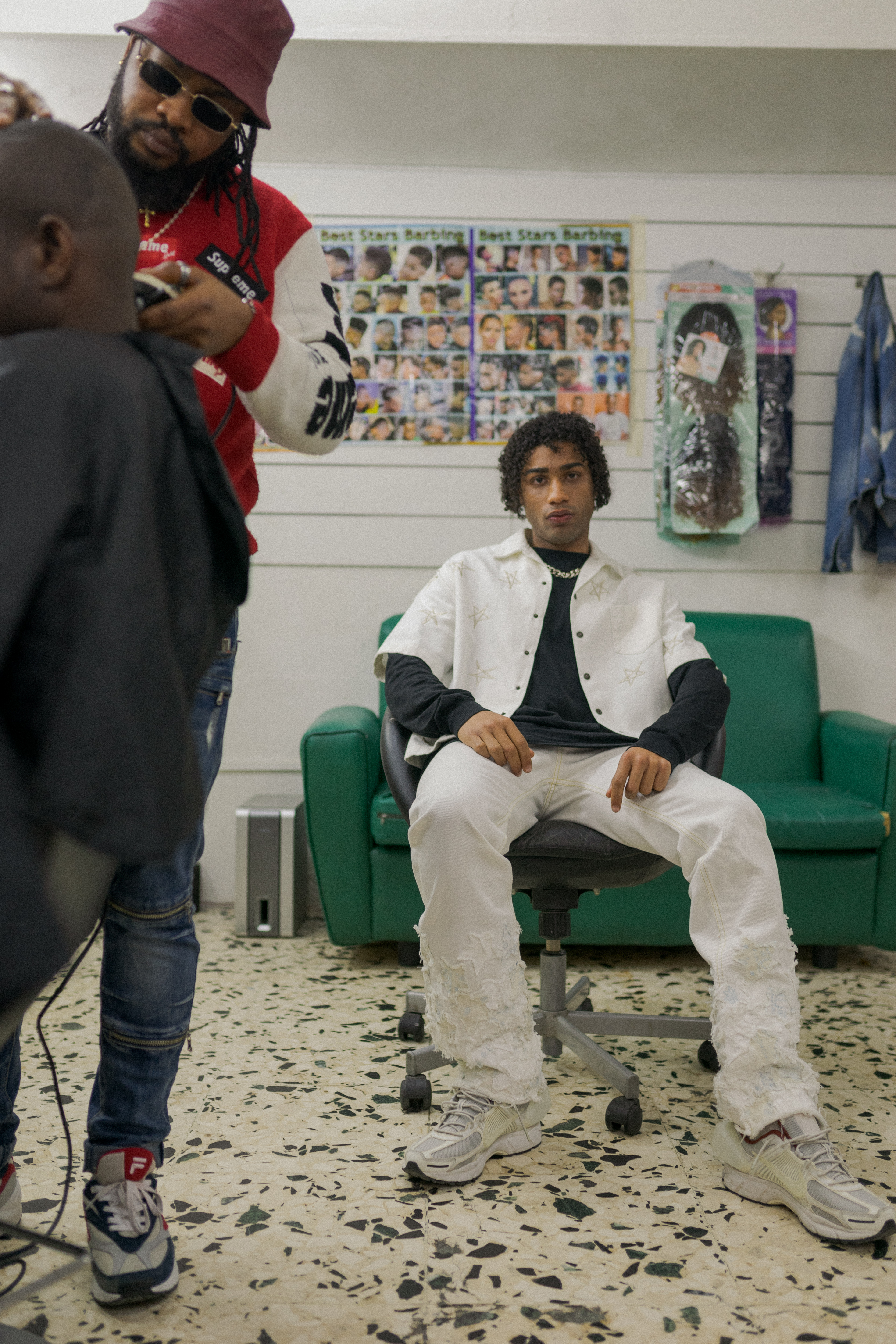 ragazzo afrodiscendente seduto sulla poltrona da barbiere mentre il barbiere taglia i capelli a qualcuno