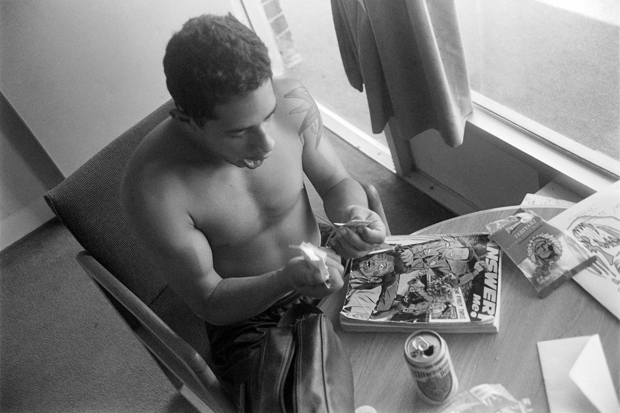 a topless man holding smoking paraphernalia over a book 