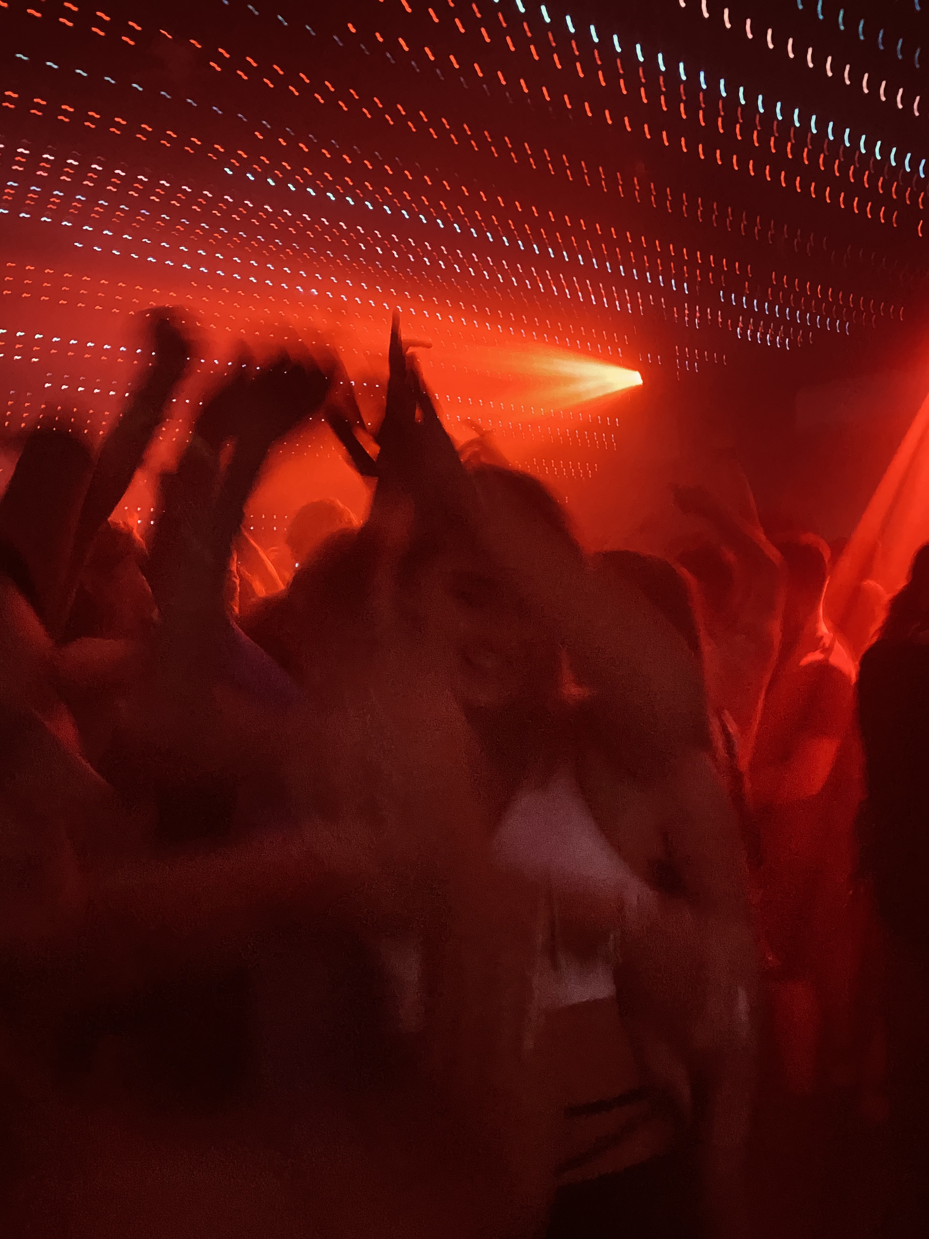 Figures dancing in a club under red and white strobe lights. 