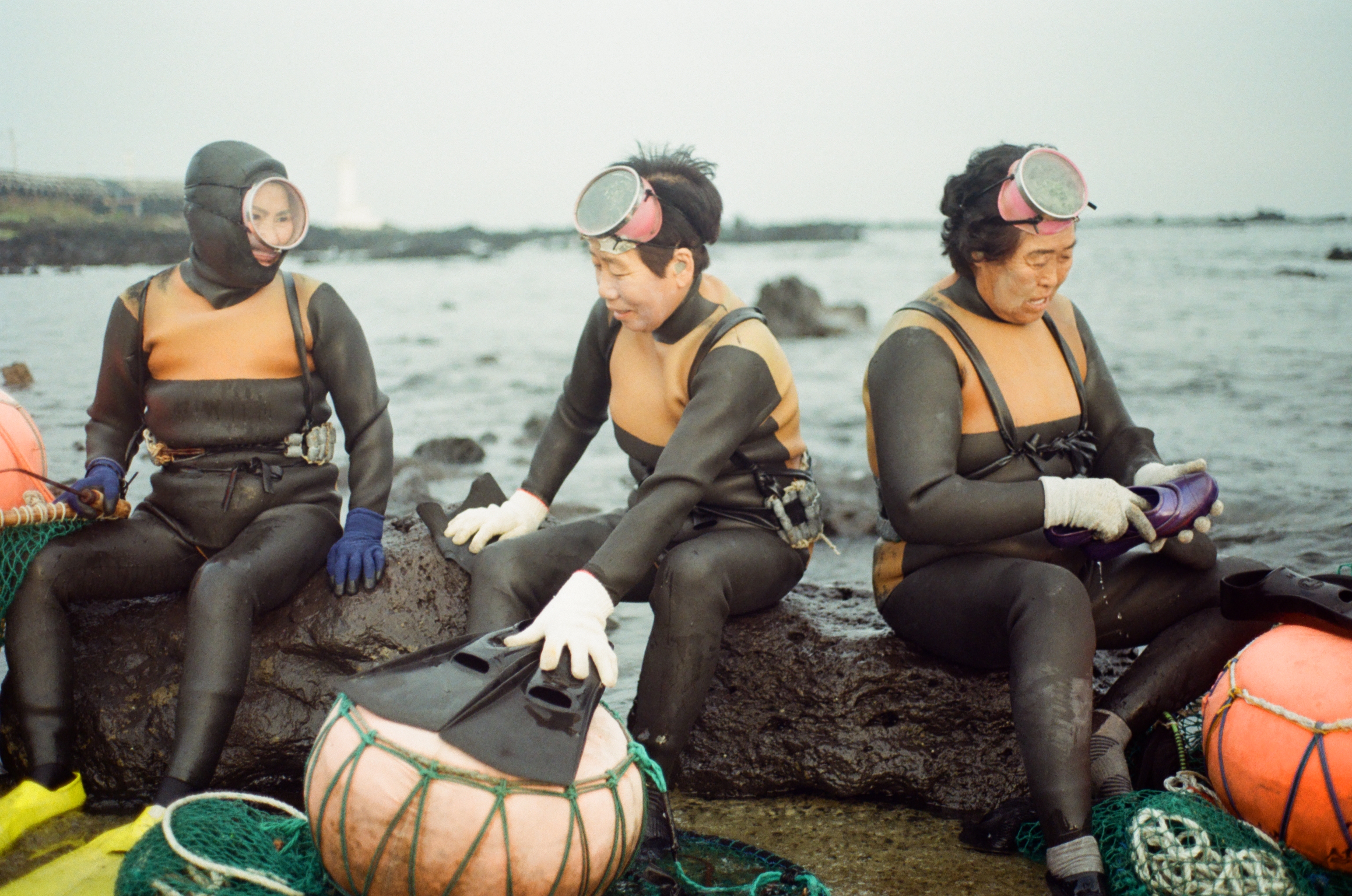 Three divers sitting on the rocks on the coast with nets around them. 