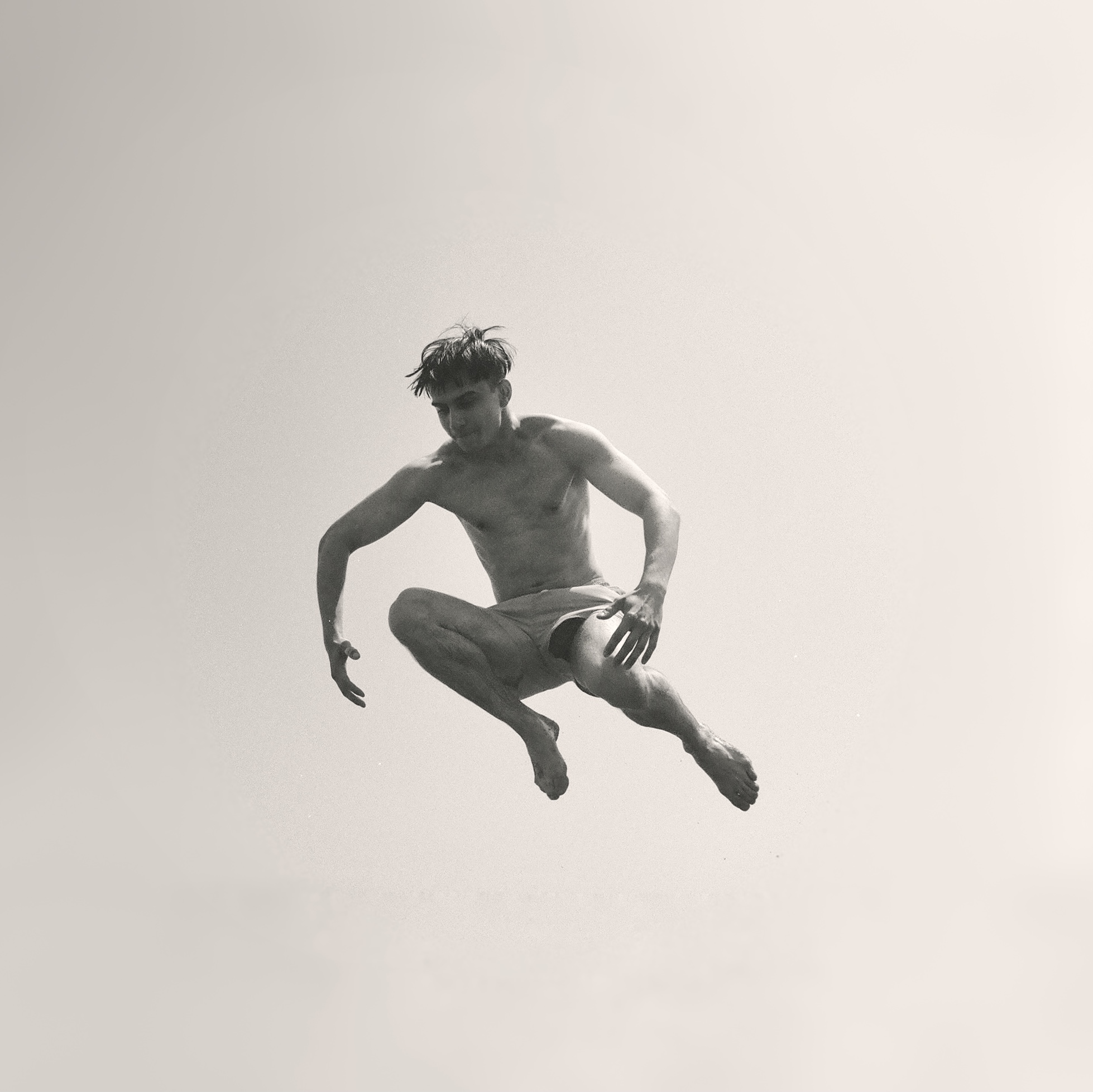 black and white photo of a boy in shorts in mid-air after jumping off a cliff.