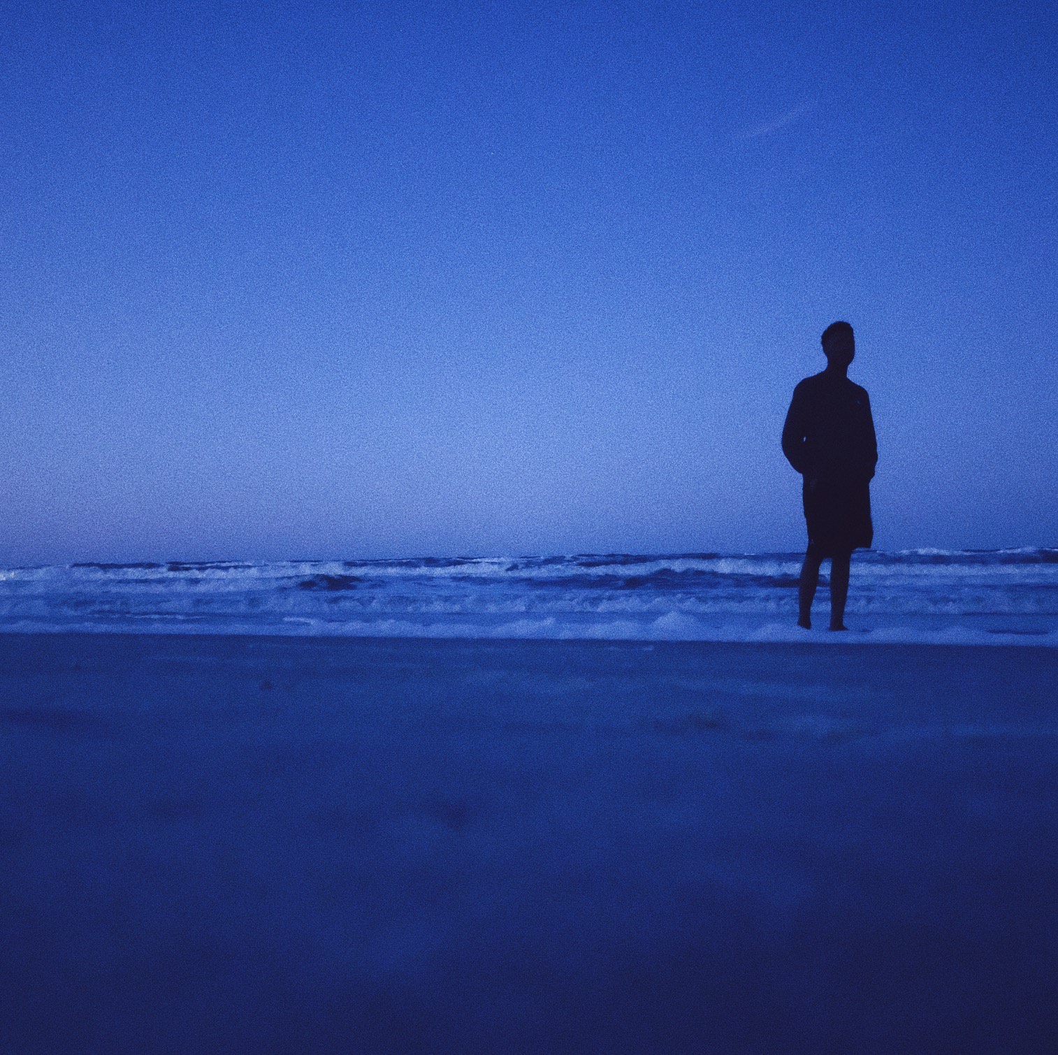 The beach during the night with the silhouette of a man on it. 
