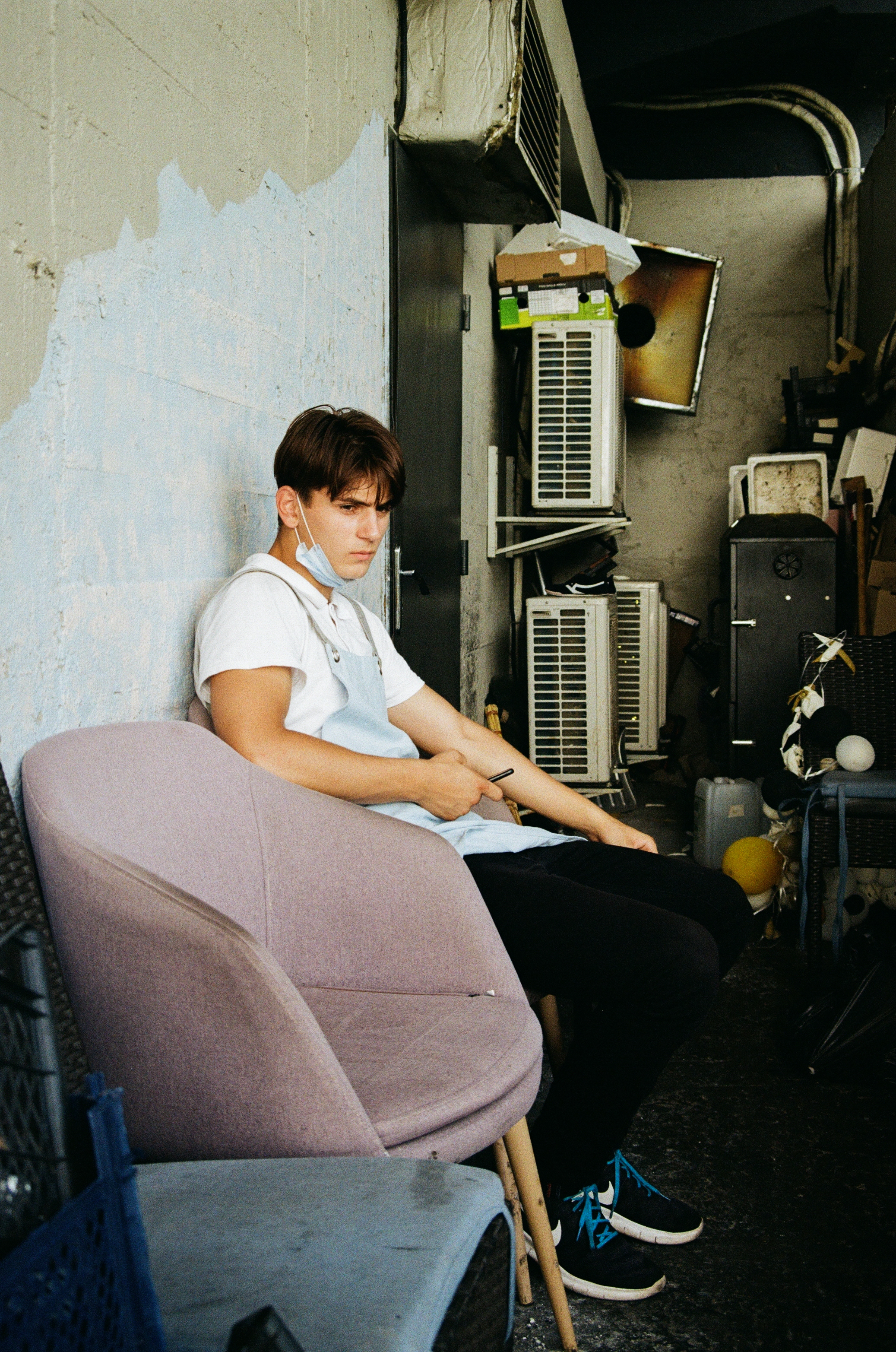 A boy in an apron sitting on a chair in front of a half painted wall.