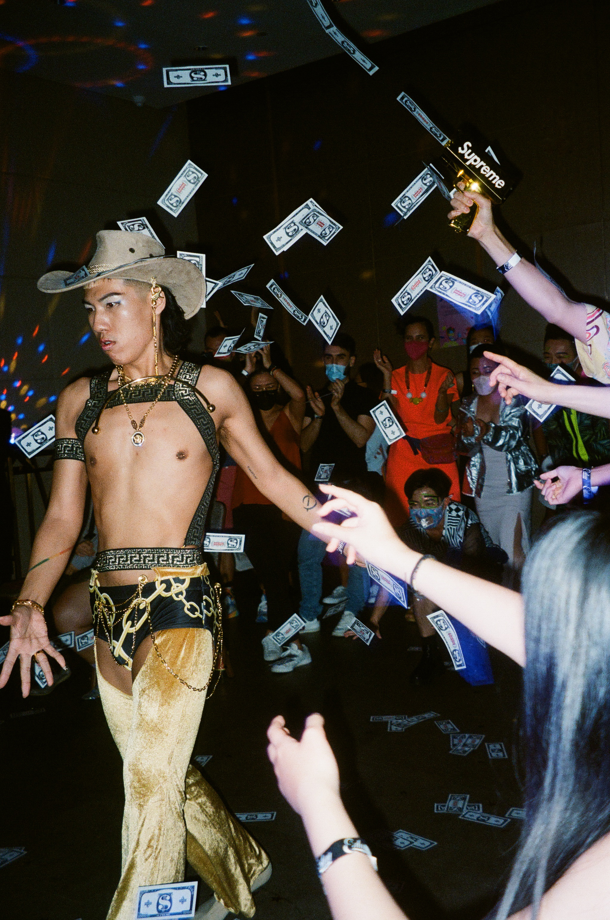 A man in gold chaps and a cowboy hat struts as money is thrown at him.