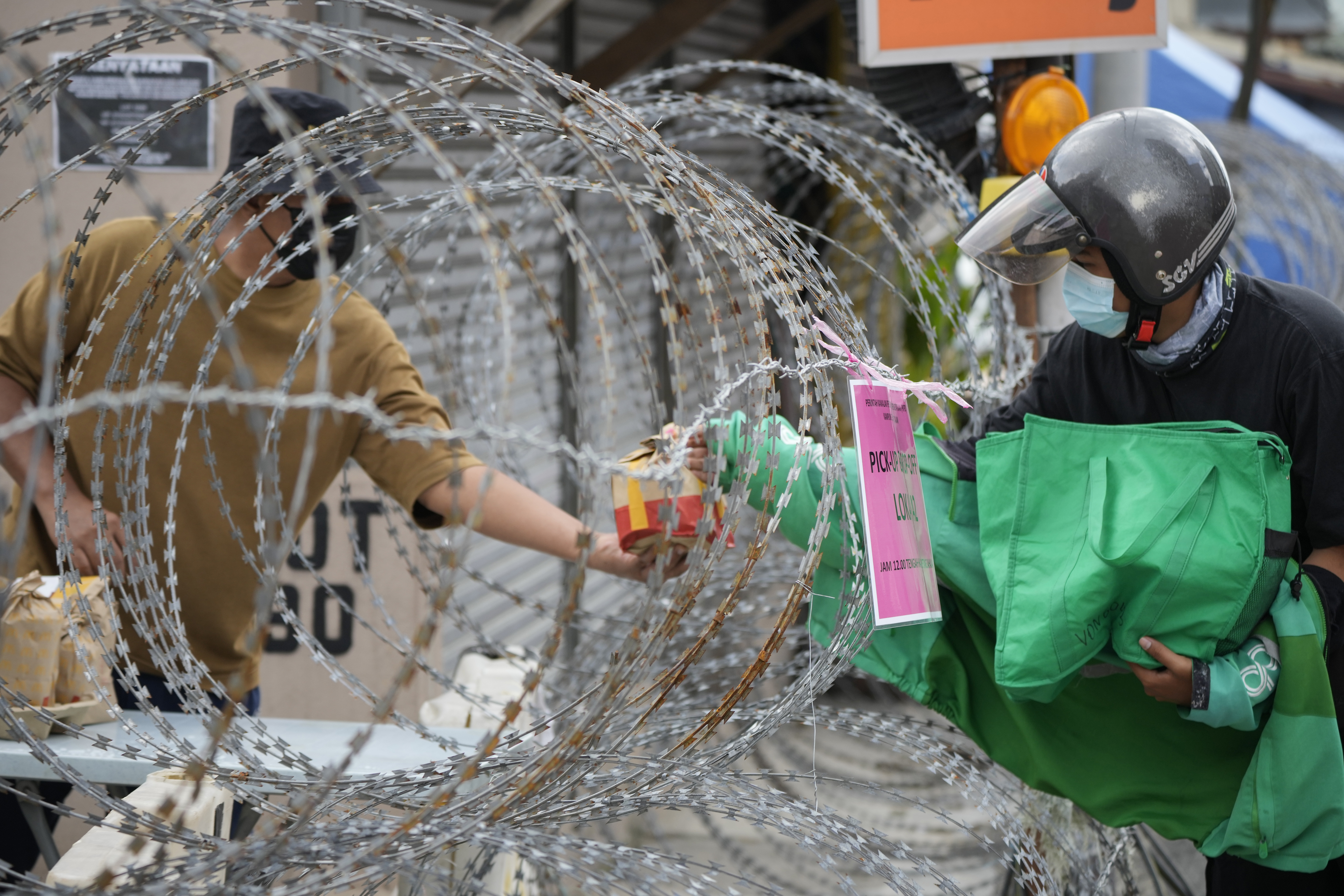 A resident in Kuala Lumpur receives food from a delivery rider through barbwire. Photo by Vincent Thian / AP