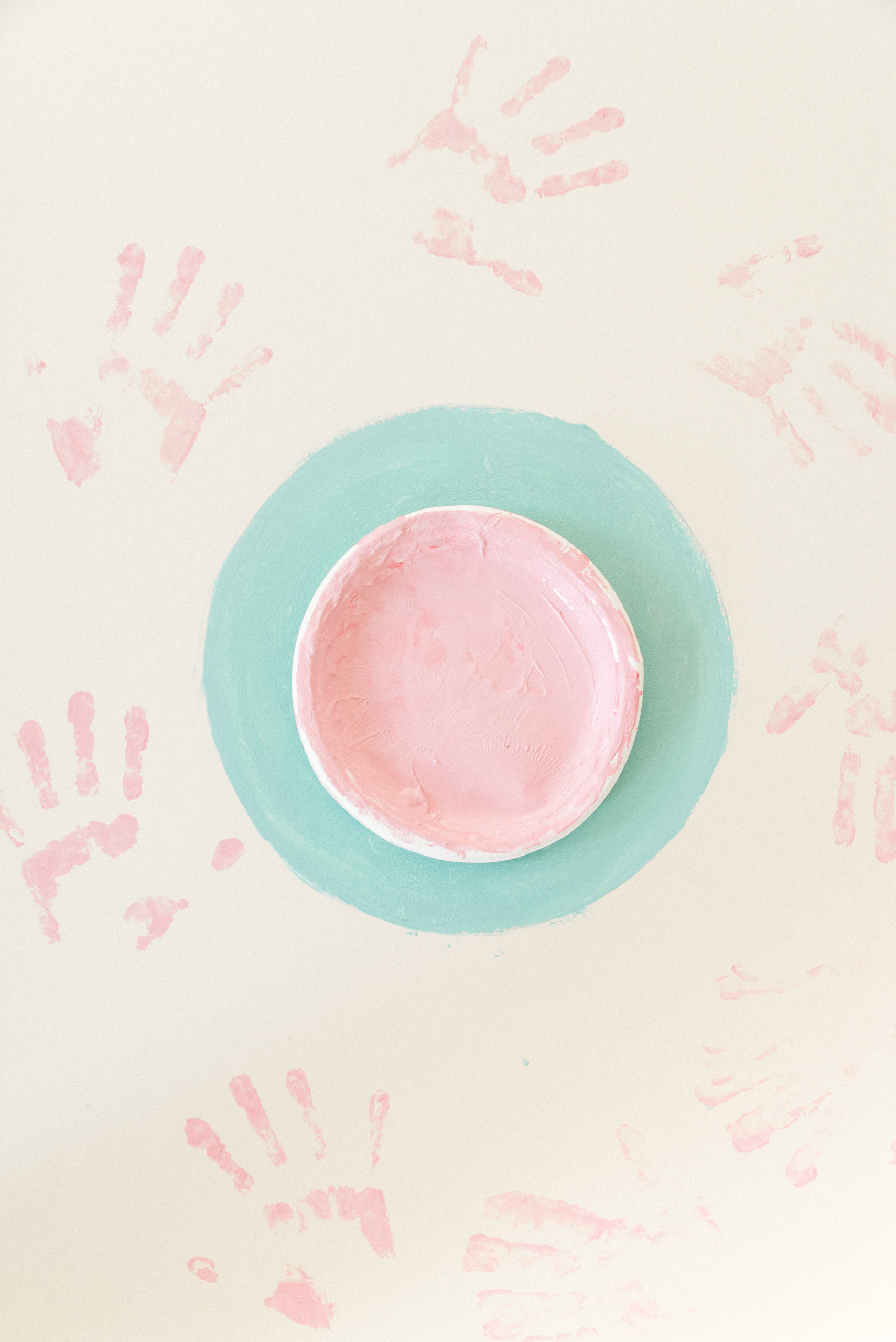 piatto rosa cìappoggiato siu cerchio azzurro e impronte di mani rosa