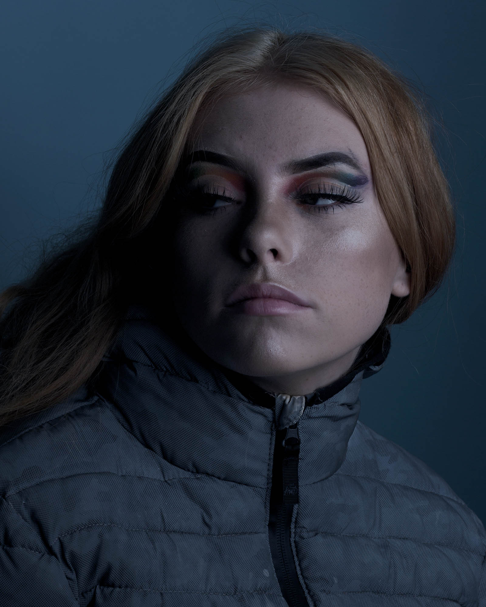 a portrait of a woman with red hair in heavy makeup wearing a puffa jacket