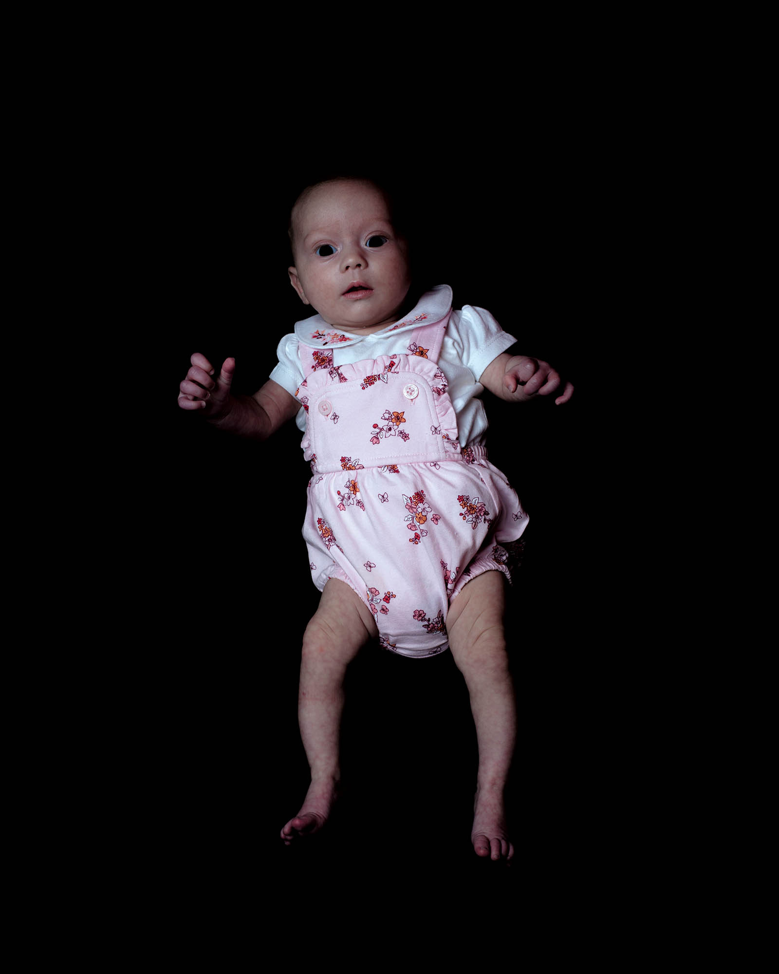 a baby is a pink outfit lying on its a back against a black backdrop