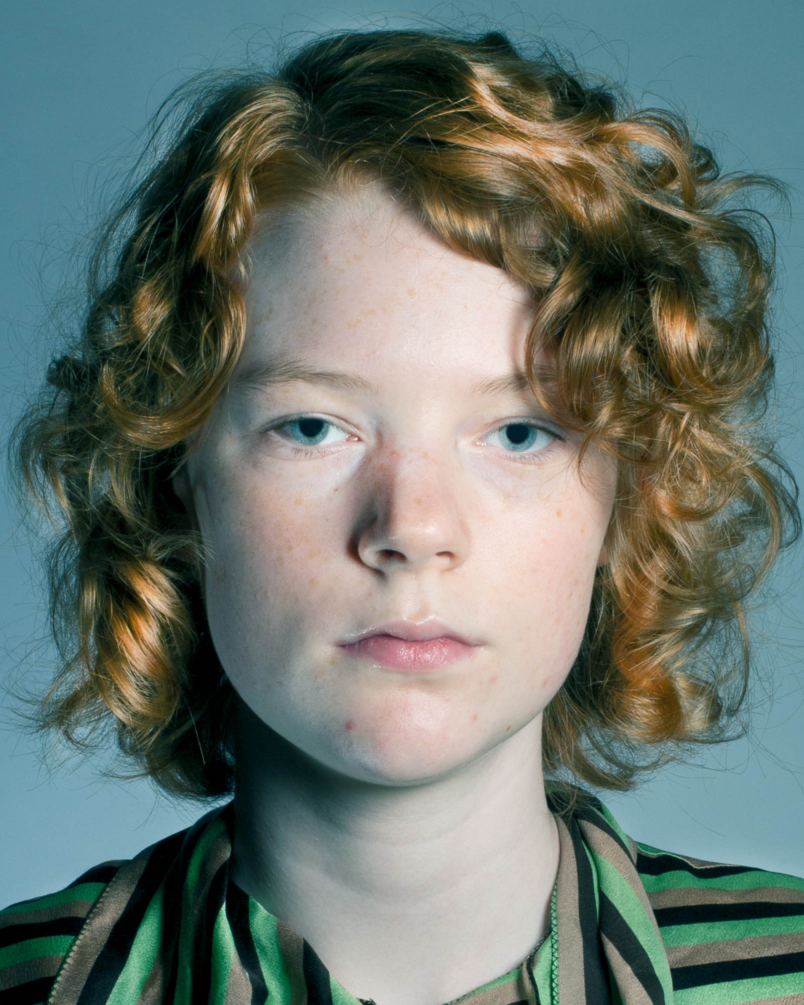 a portrait of a red haired person in a stripy shirt against a pale blue backdrop