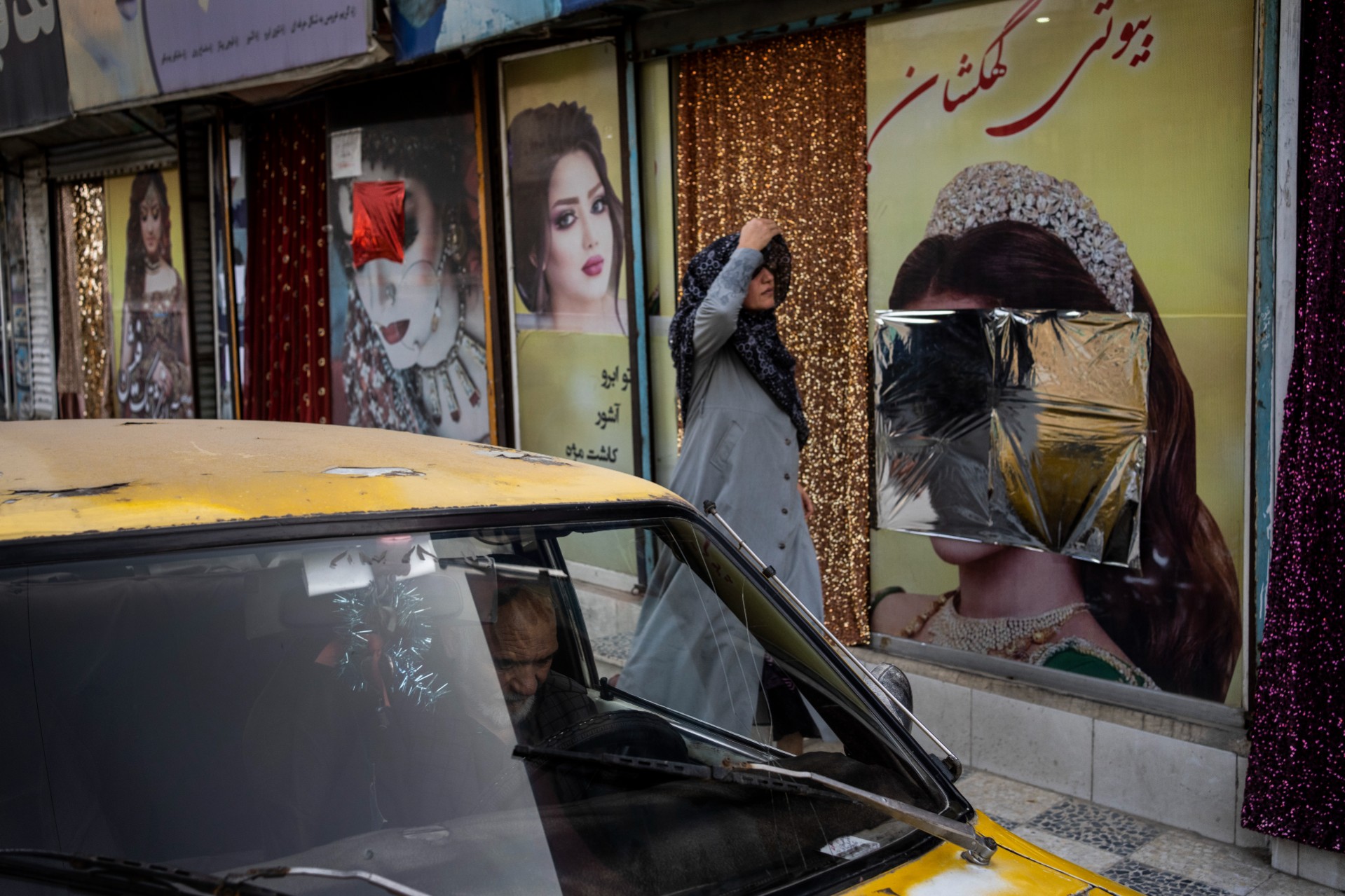 Perempuan Afghanistan berjalan di depan salon kecantikan. Poster perempuan yang terpajang di luar salon telah ditutupi awal bulan ini. Foto: AP Photo/Bernat Armangue