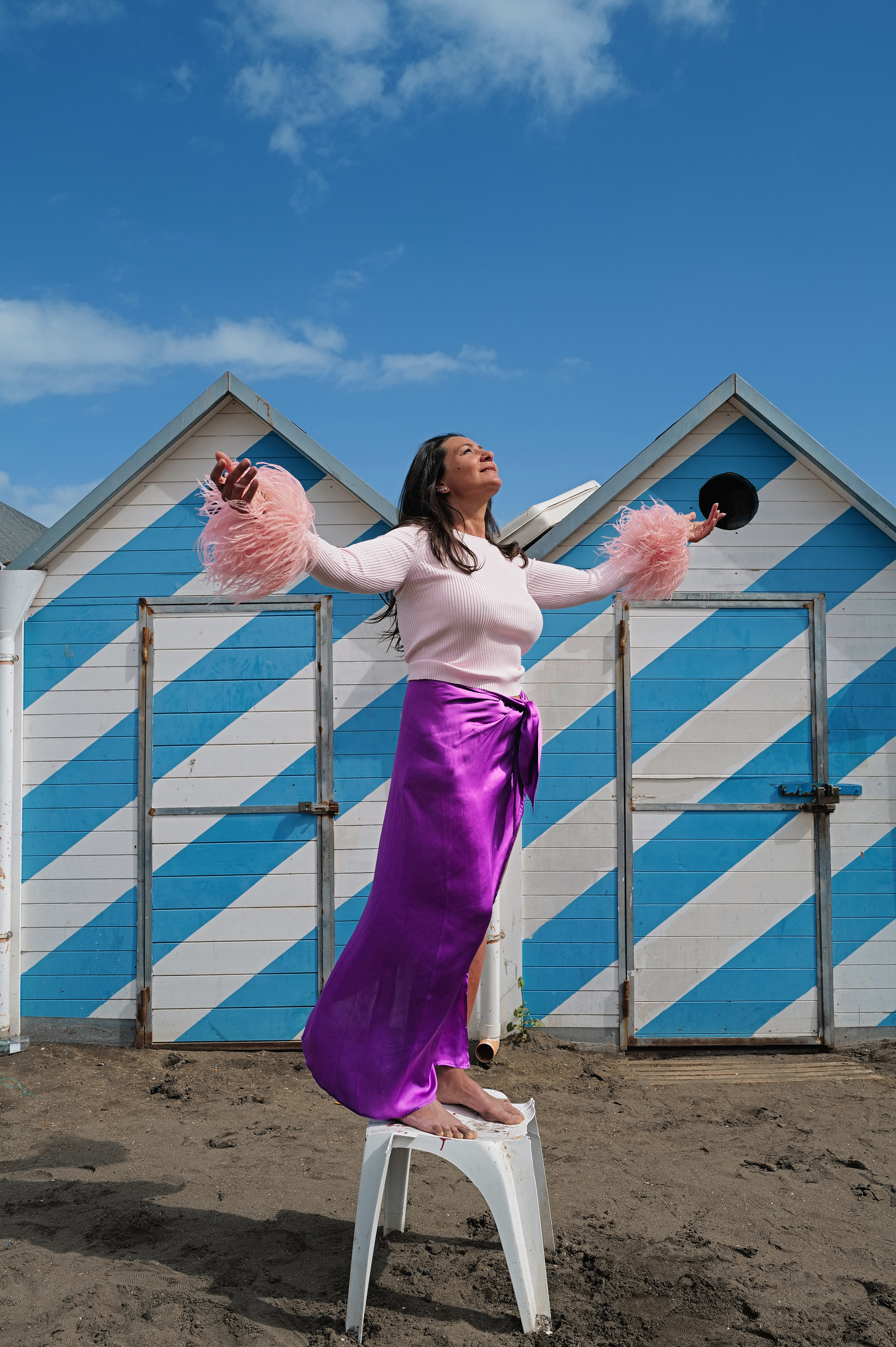donna in abito rosa e viola di fronte a delle cabine da spiaggia