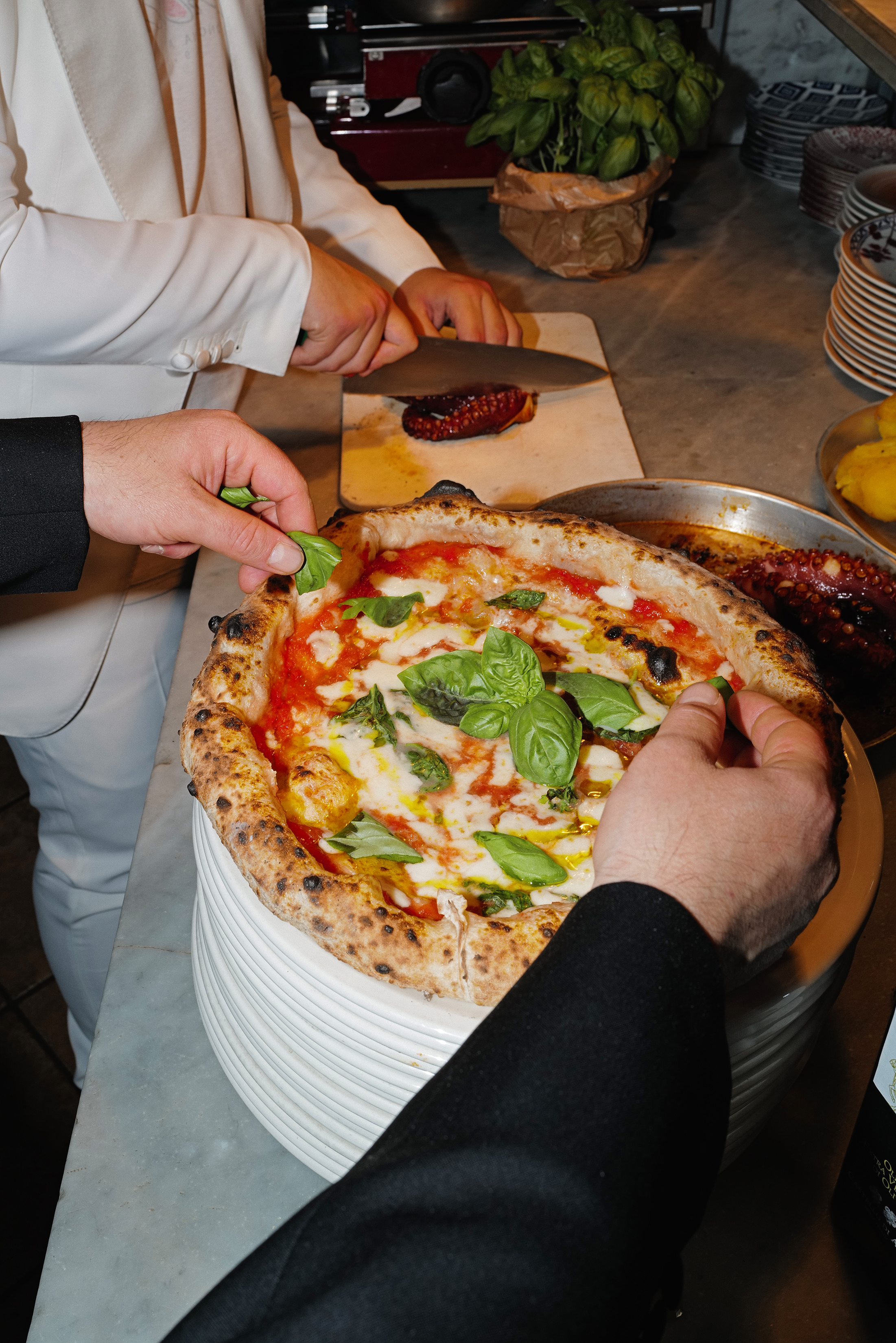 chef che impiatta una pizza con del basilico