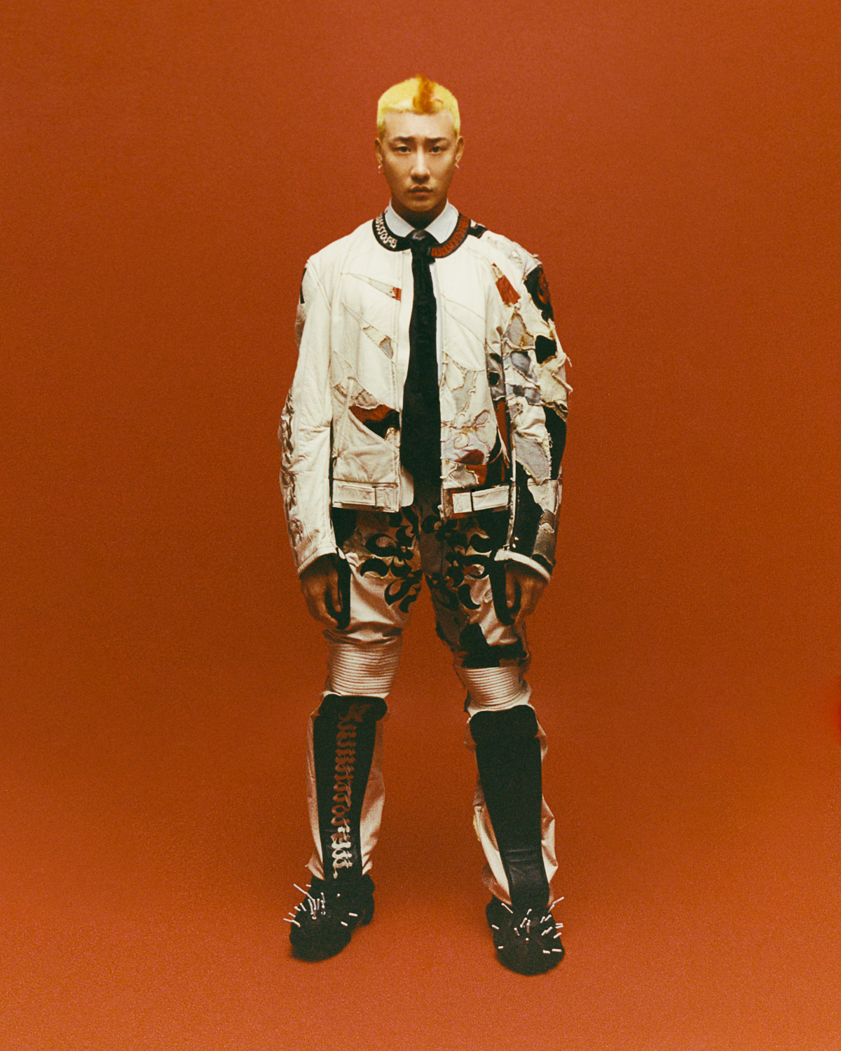 a portrait of a person with bleached hair wearing a worn leather biker jacket on a red background