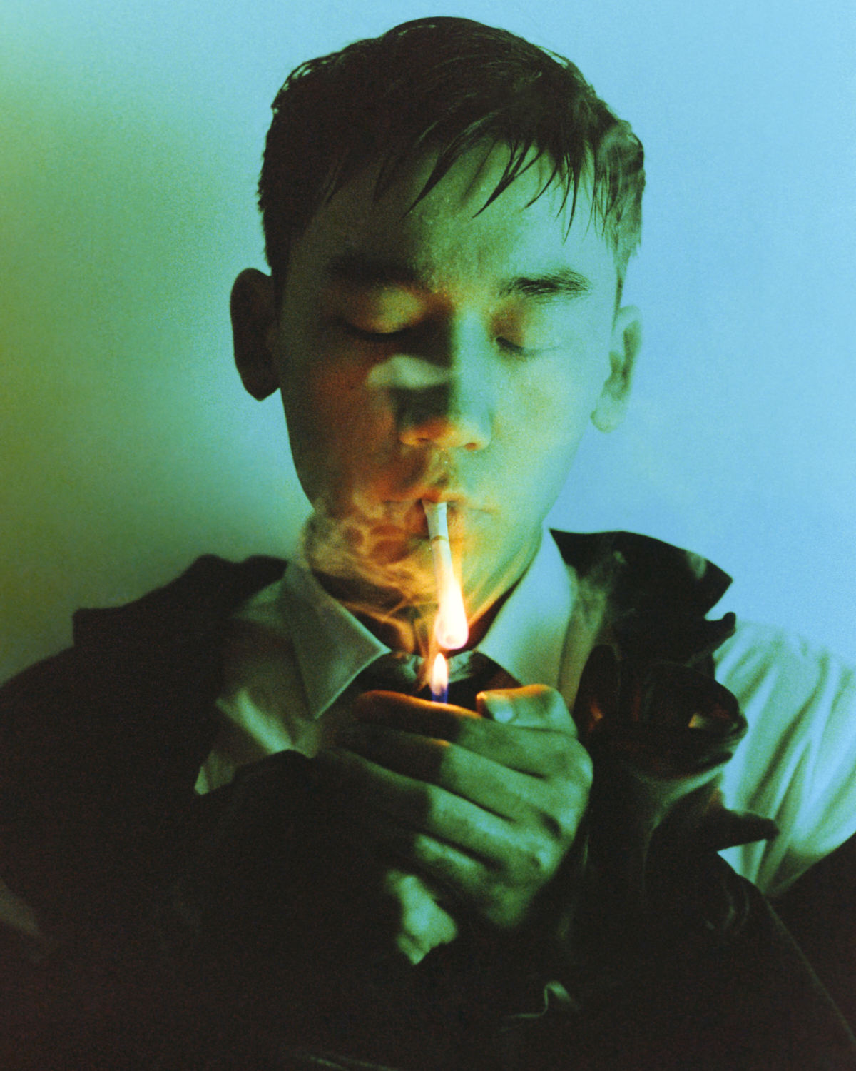 a man lights a cigarette under blue coloured light