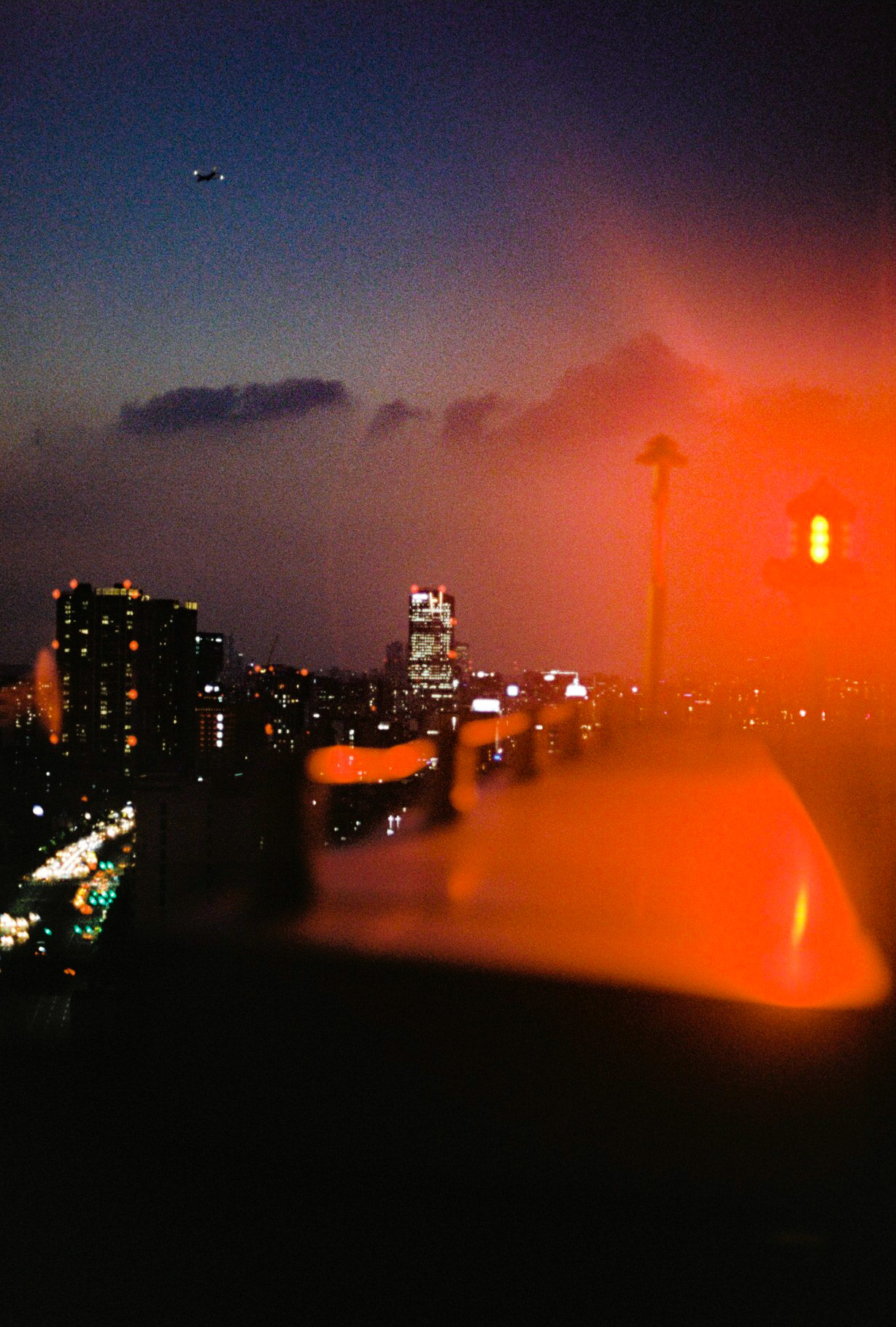 view of Seoul city skyline at night, the buildings and road lit up and highlighted by the flares of a red plane signal light.