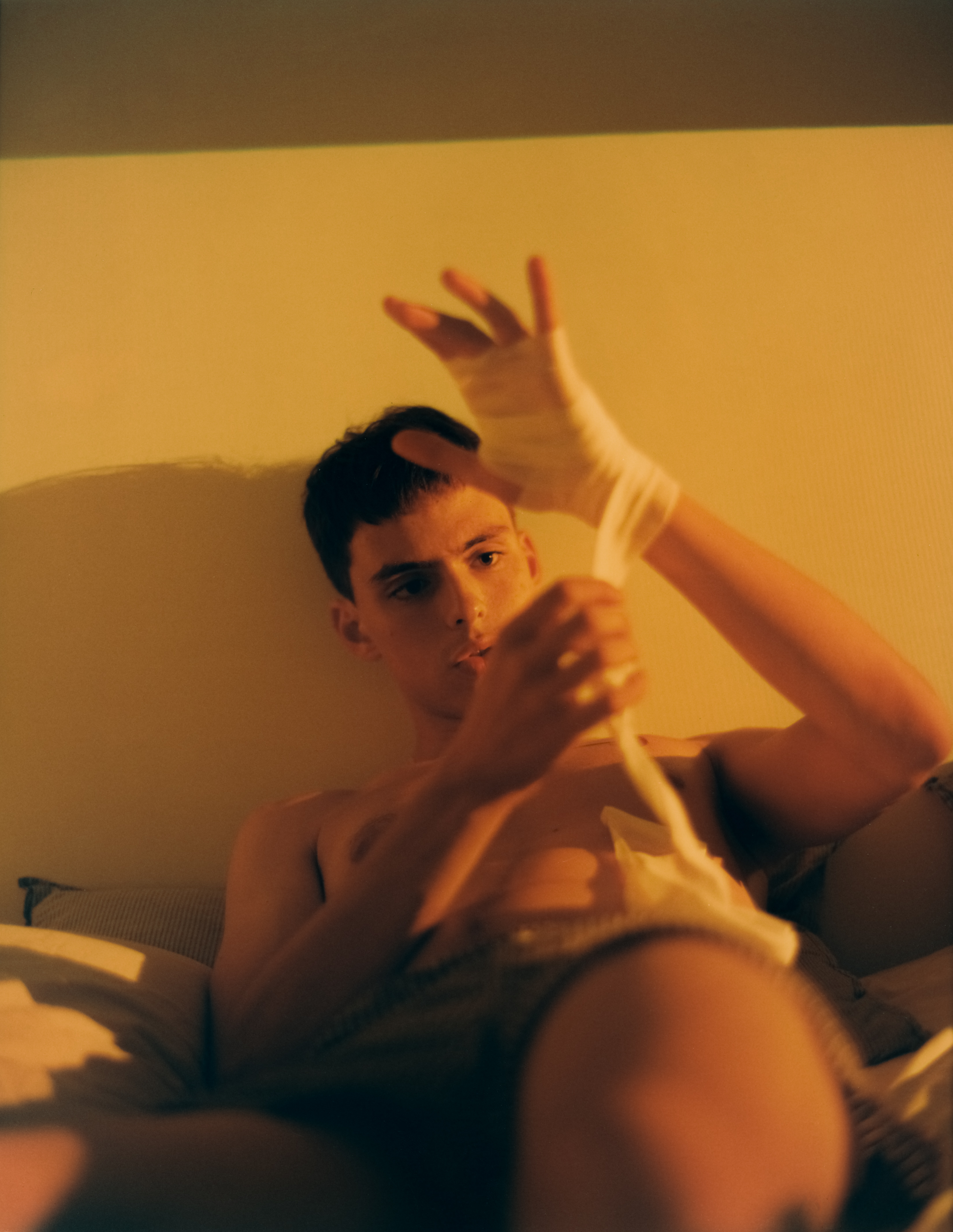 Boy lays in bed and bandages hand. 