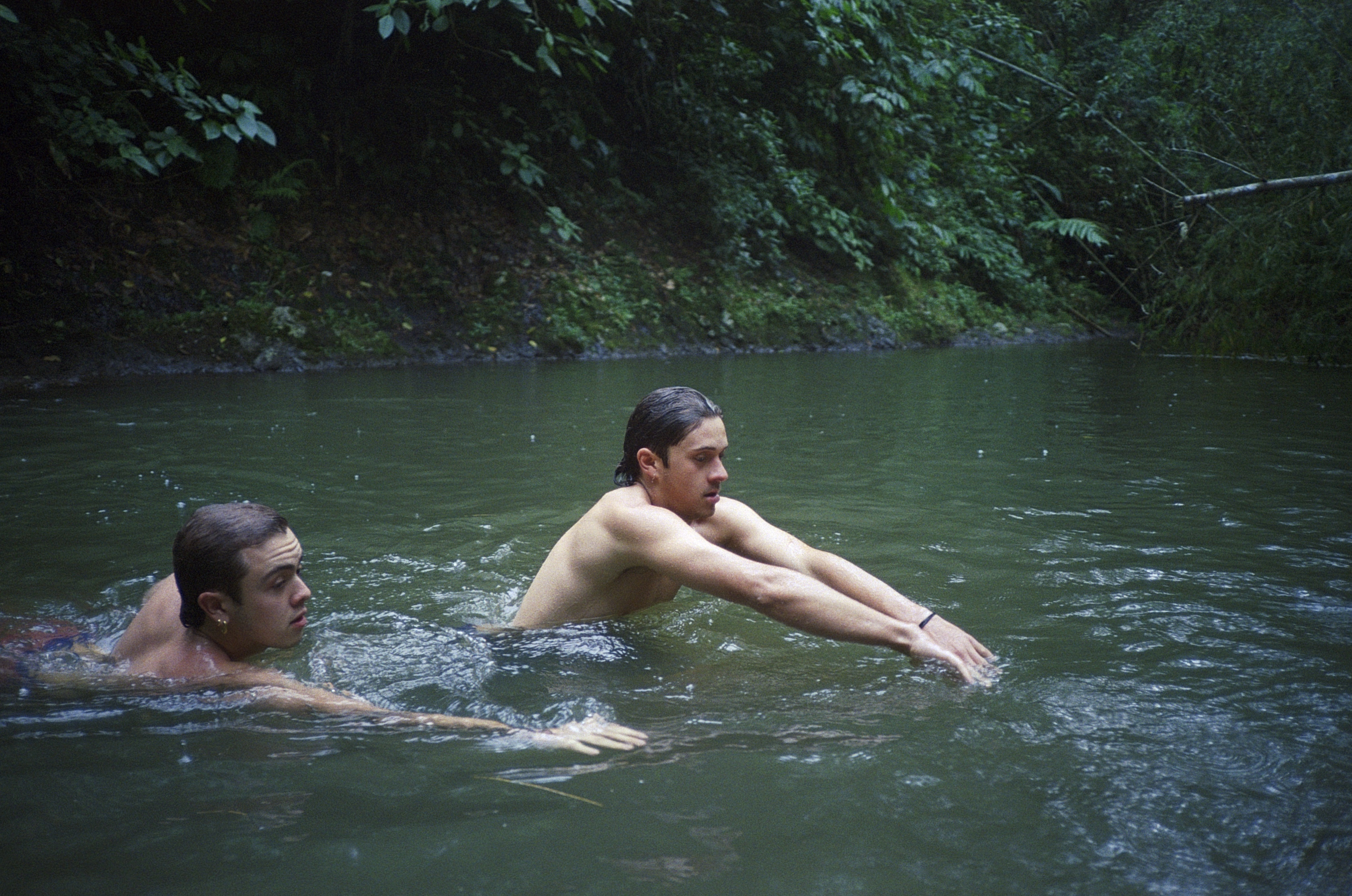 Two boys swim in a lake surrounded by trees