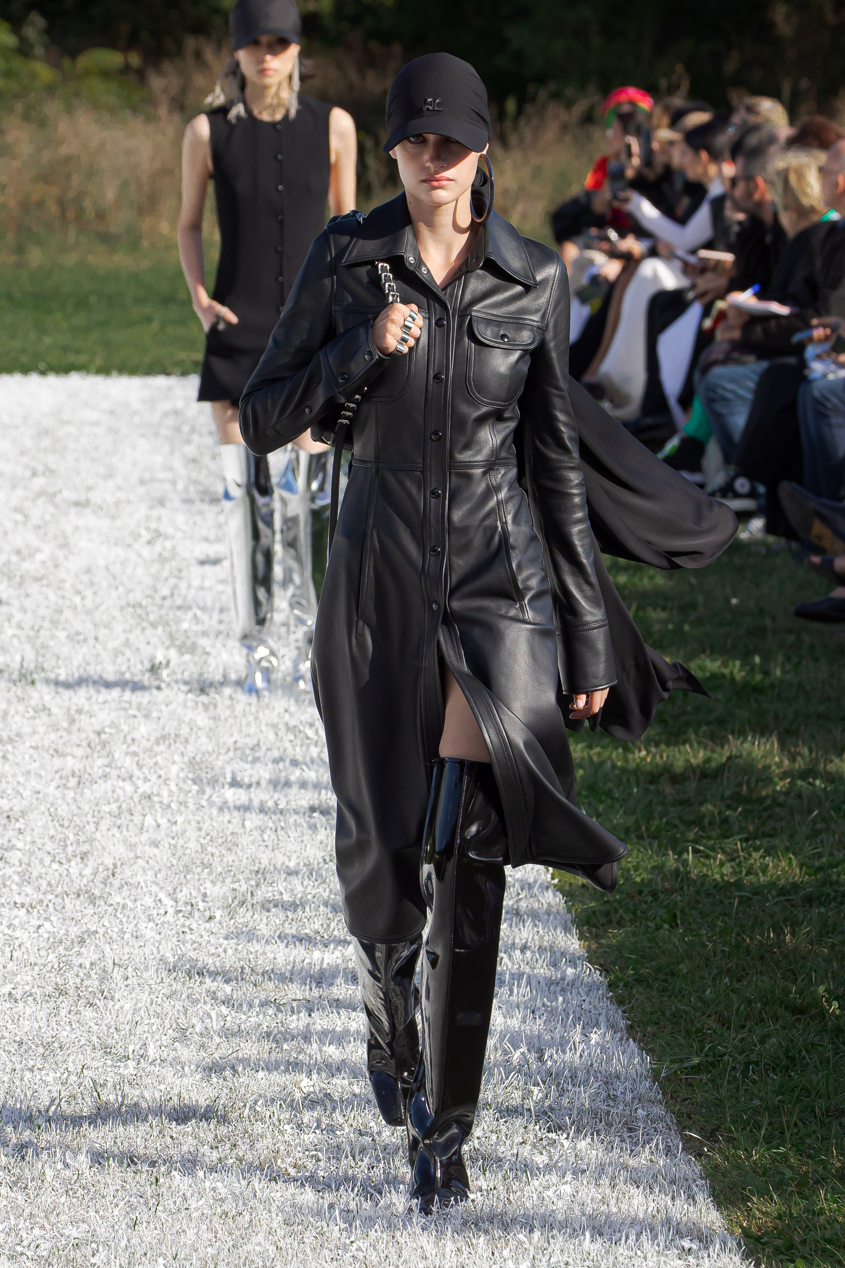 Courreges SS22 catwalk look: a model wears a long black leather coat with thigh-high boots and a cap
