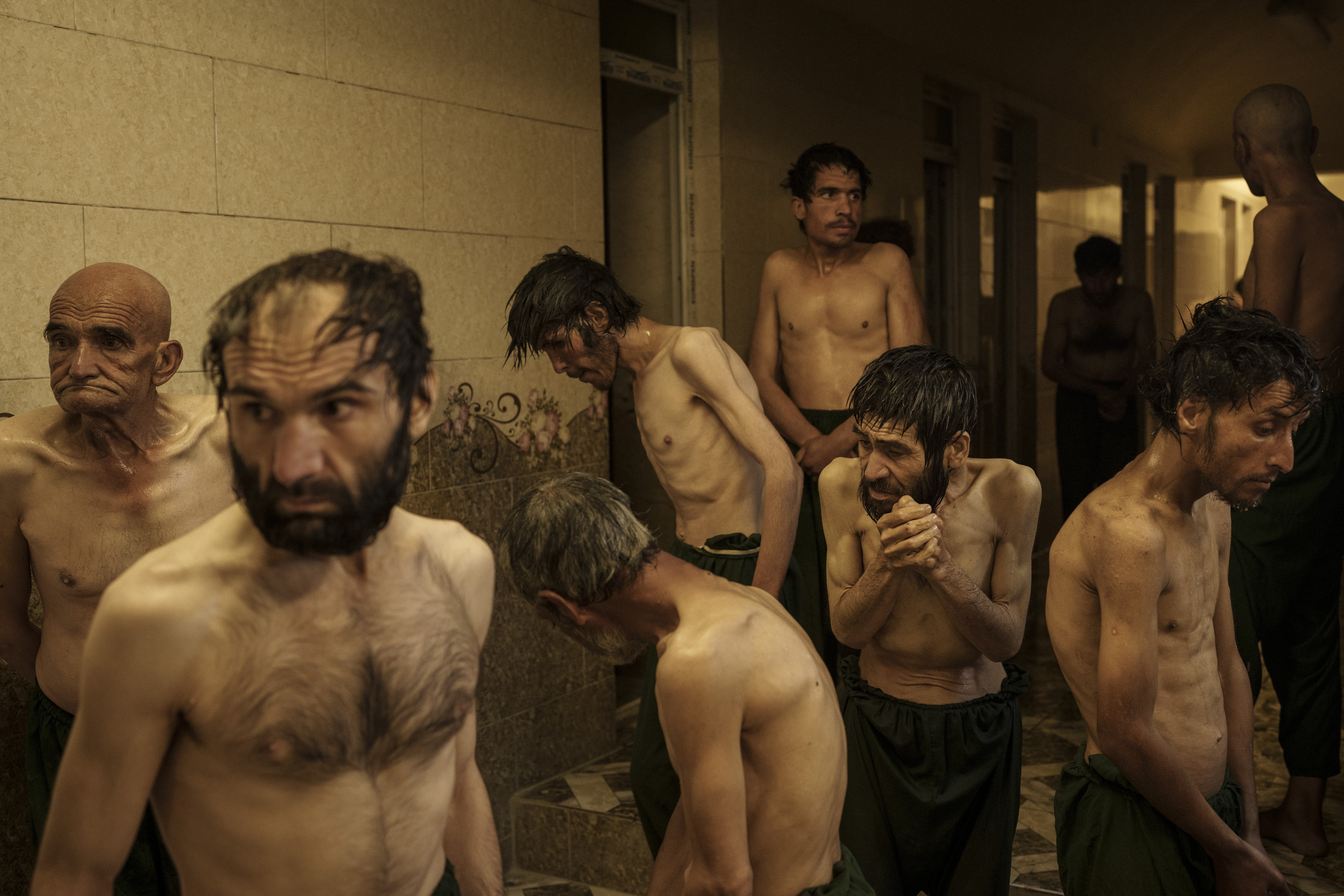 Tujuh lelaki bertelanjang dada menunggu giliran cukur rambut setelah mandi.