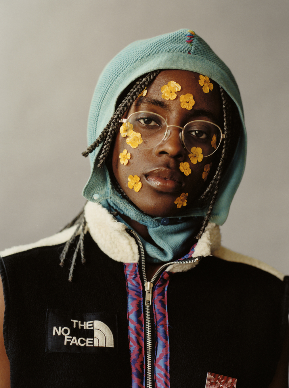 Lola + Pani photograph of a model wearing a customised north face fleece with a knit balaclava and yellow pressed buttercups on their face 
