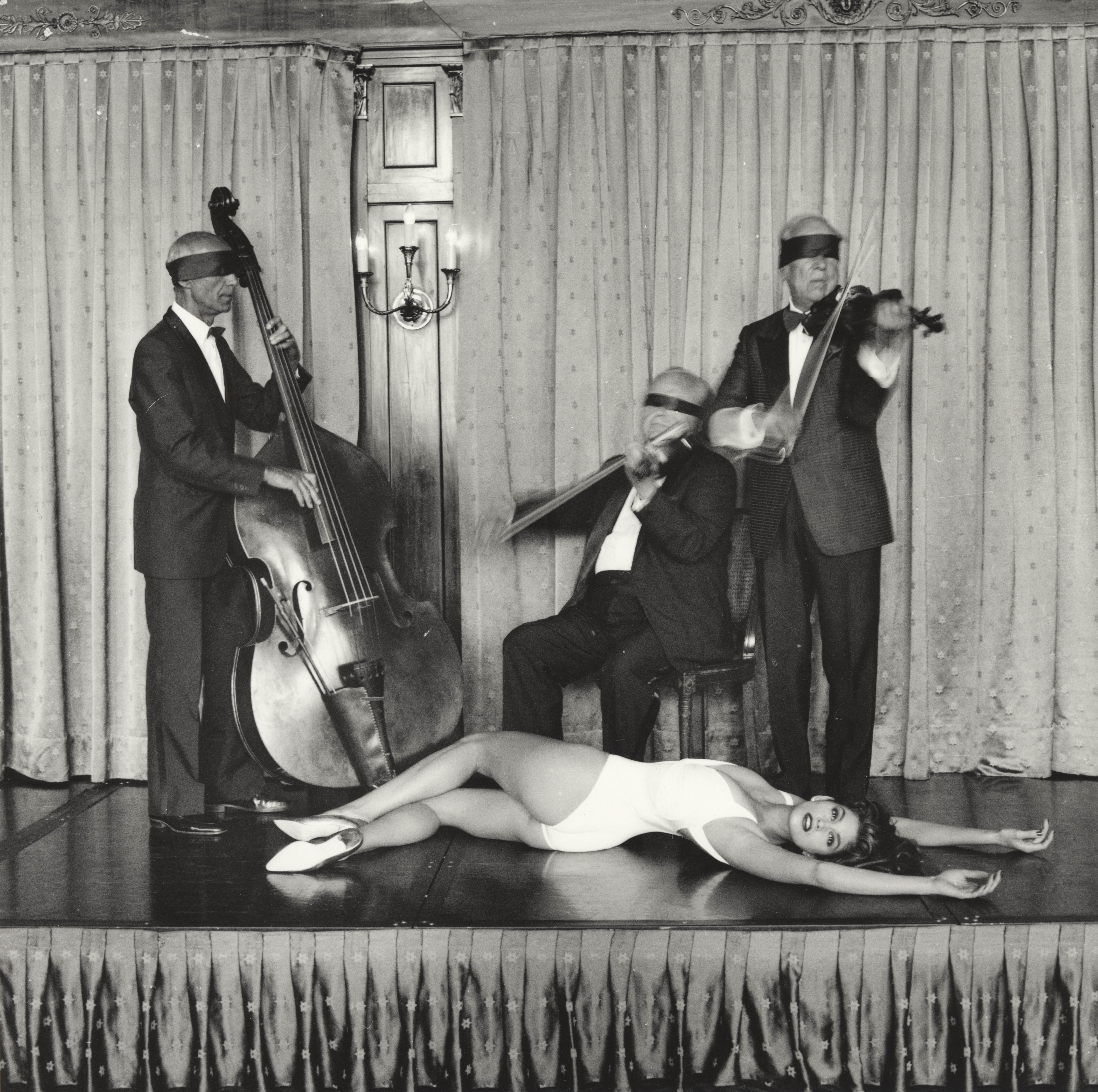 a model lies on a stage in front of a band playing with blindfolds